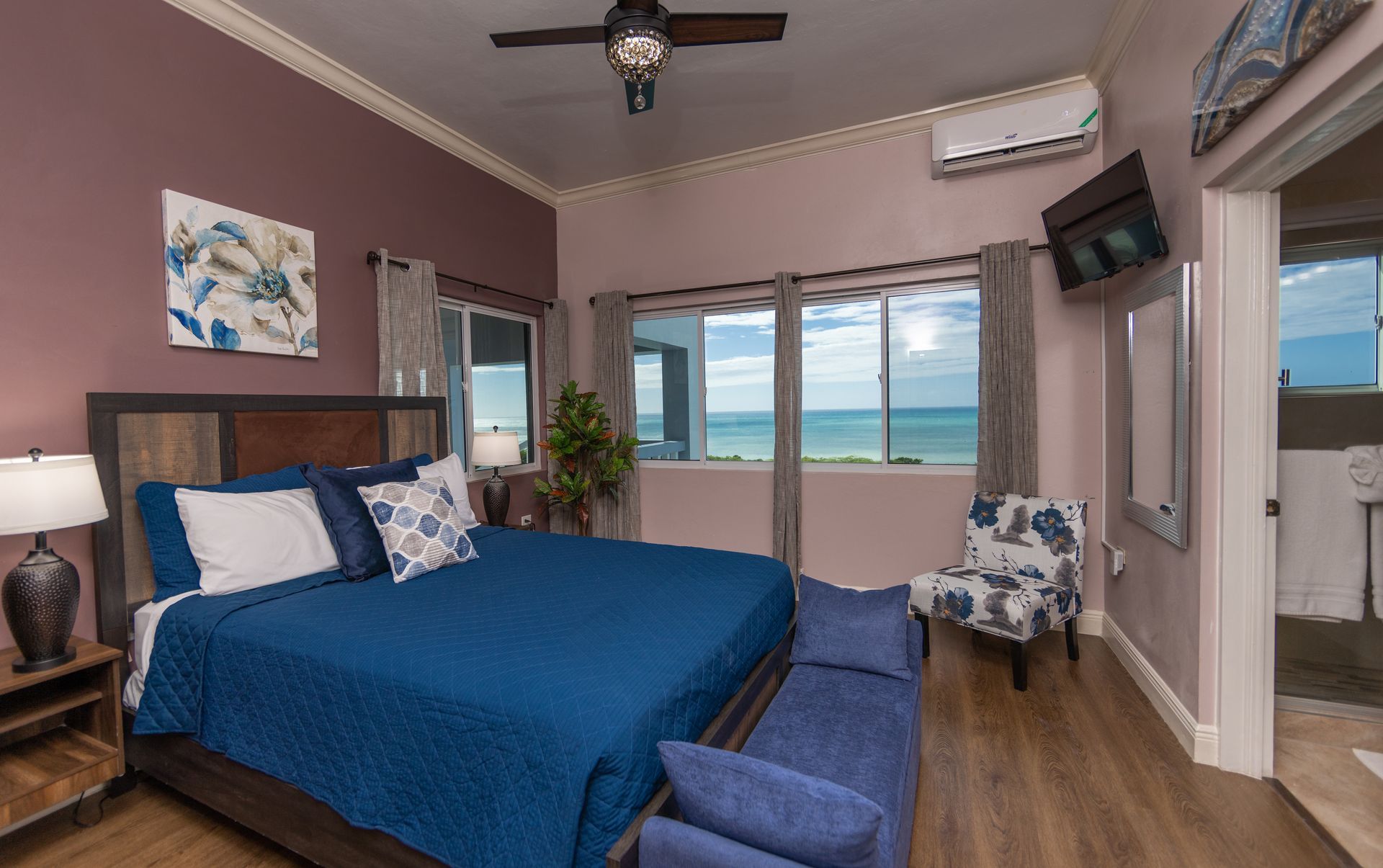 Bedroom with ocean view, blue bedspread, floral accent chair, and air conditioner.