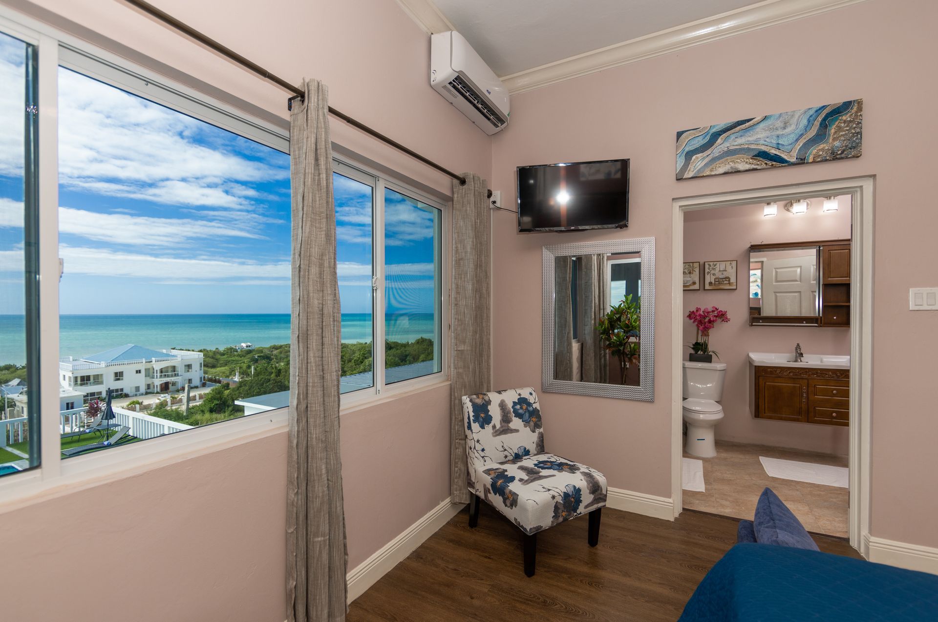 Bedroom with ocean view, windows, chair, TV, and open bathroom doorway.