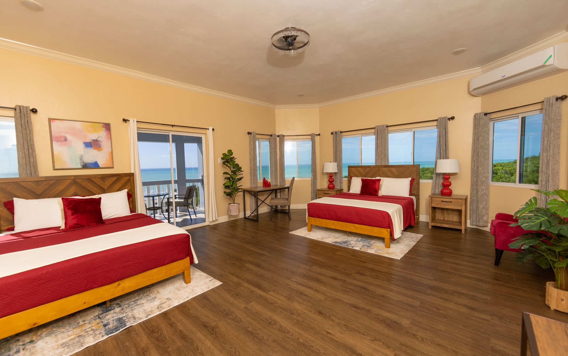 Spacious bedroom with two queen beds, sea views, wooden floors, and red and white bedding.