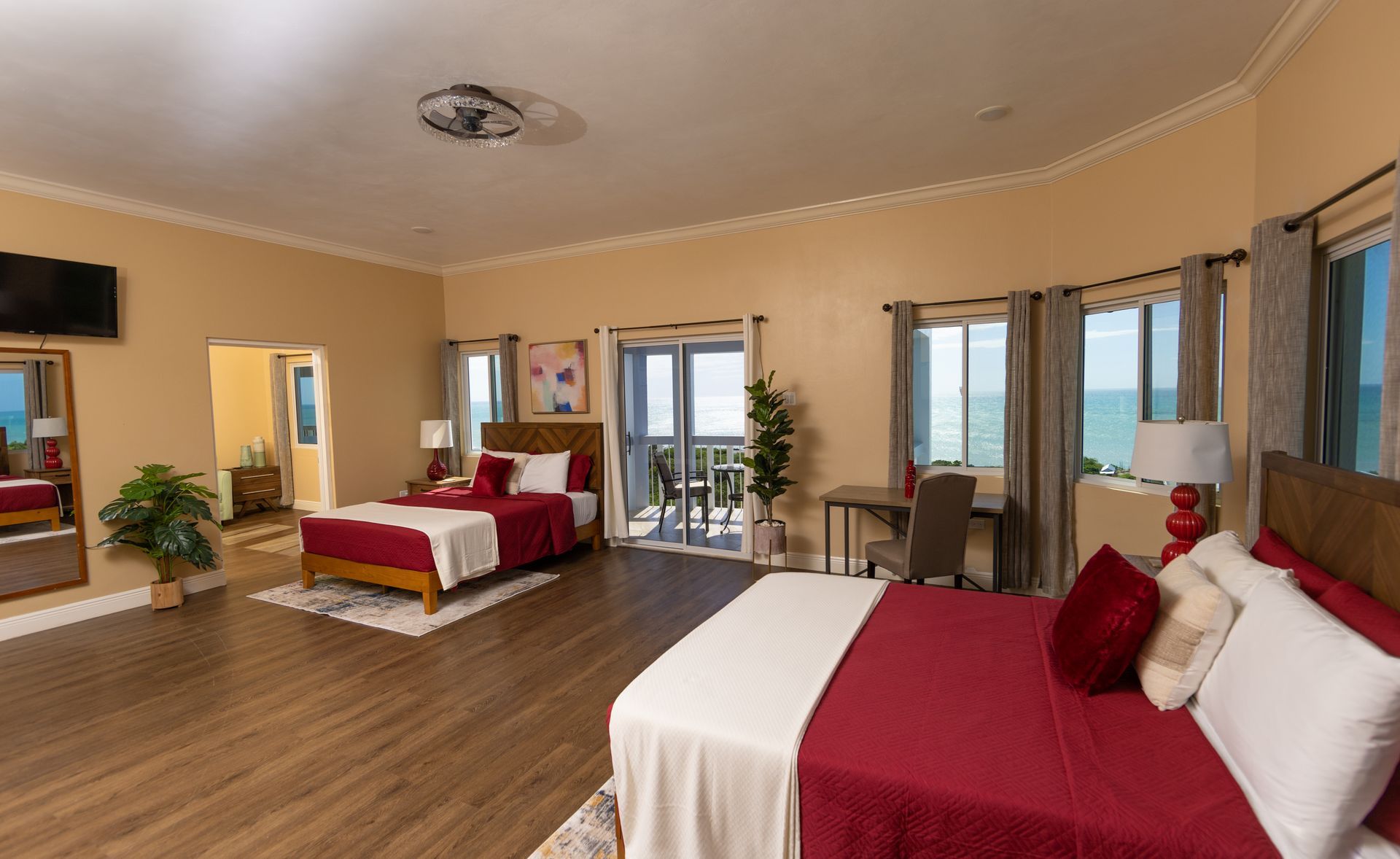 Large bedroom with two beds, red bedding, ocean view from balcony and windows.