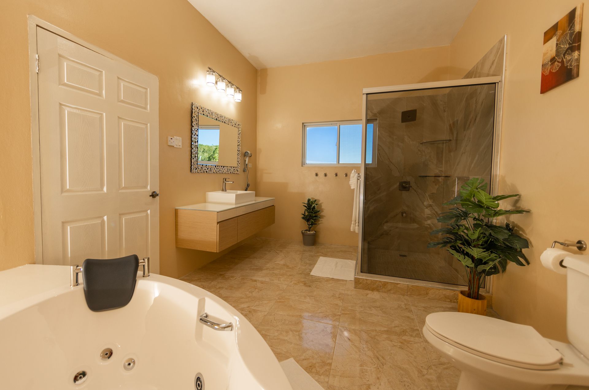 Bathroom with beige walls, a white tub, shower, and toilet. A vanity with a mirror is on the wall.