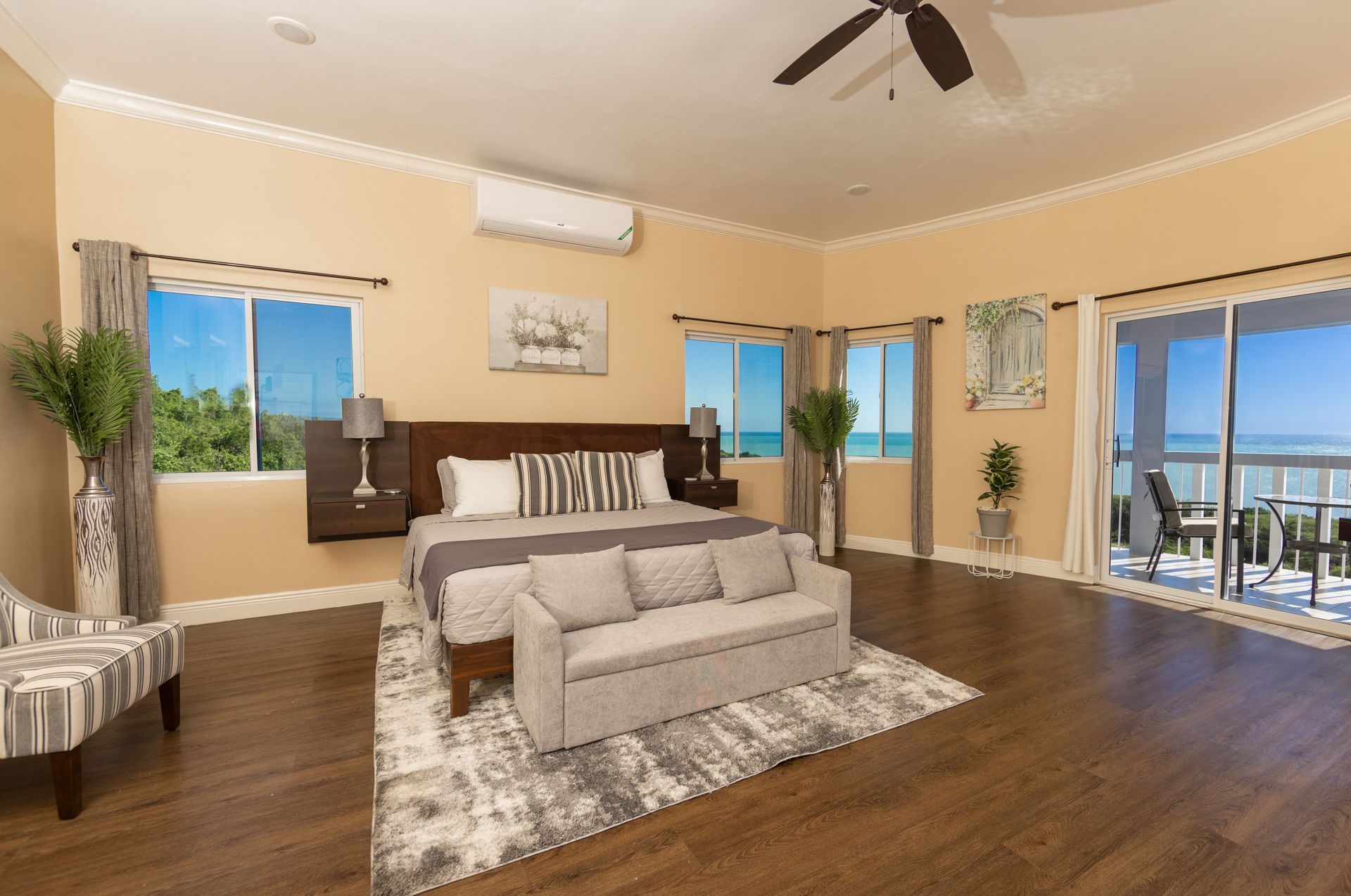 Spacious bedroom with ocean view. Brown wood floors, cream walls, king bed, seating area, and sliding glass doors.