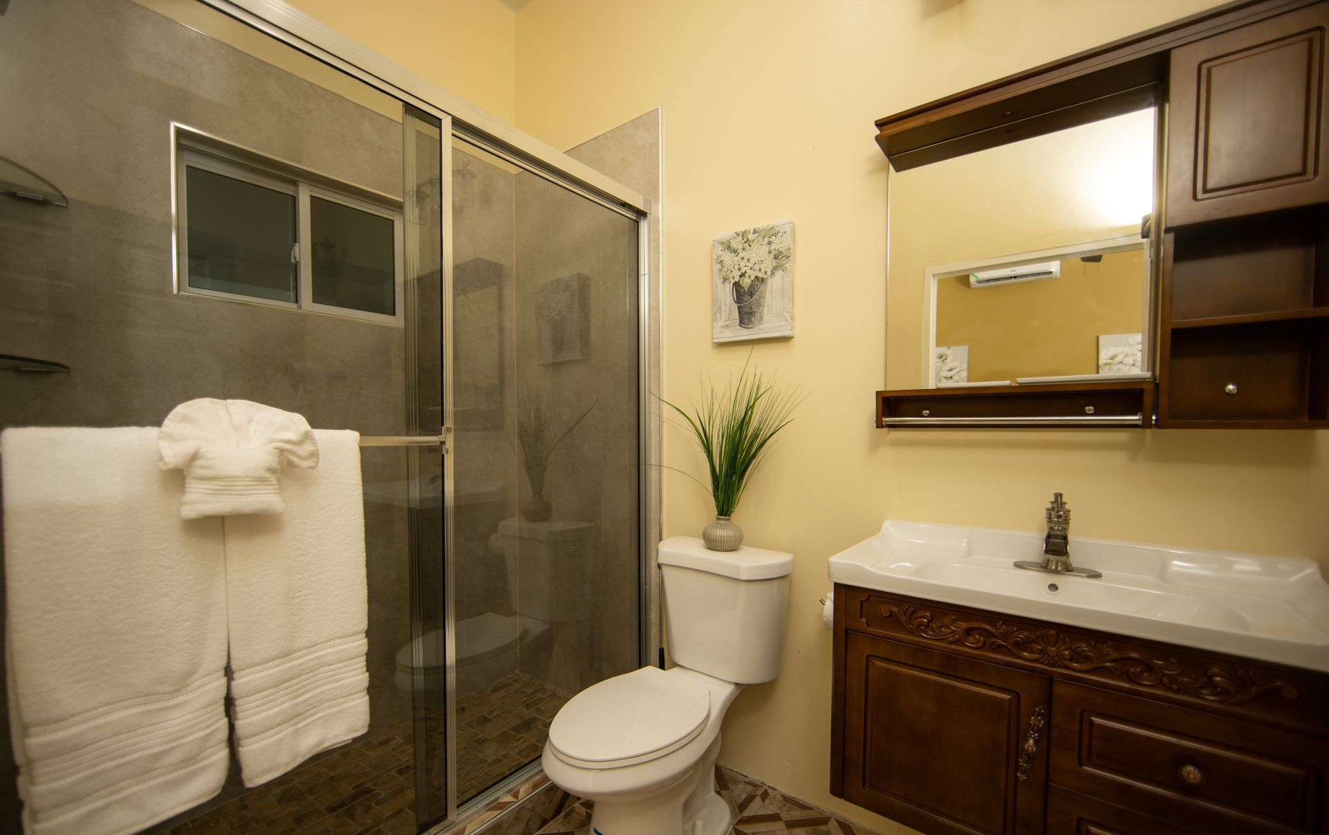 Bathroom with a shower, toilet, and vanity. Beige walls, brown cabinets, and white towels.