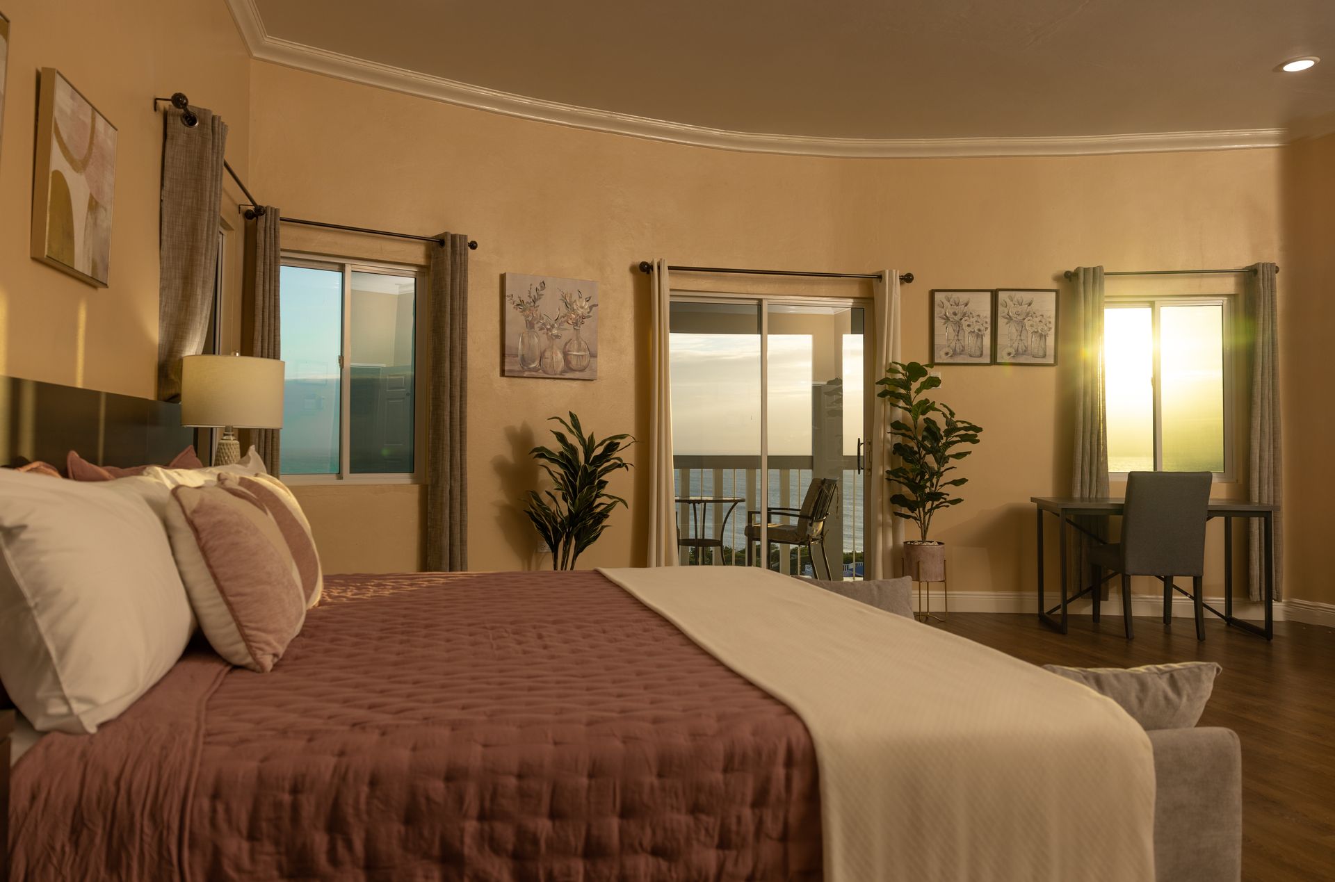Bedroom with bed, windows, and balcony, bathed in sunlight.