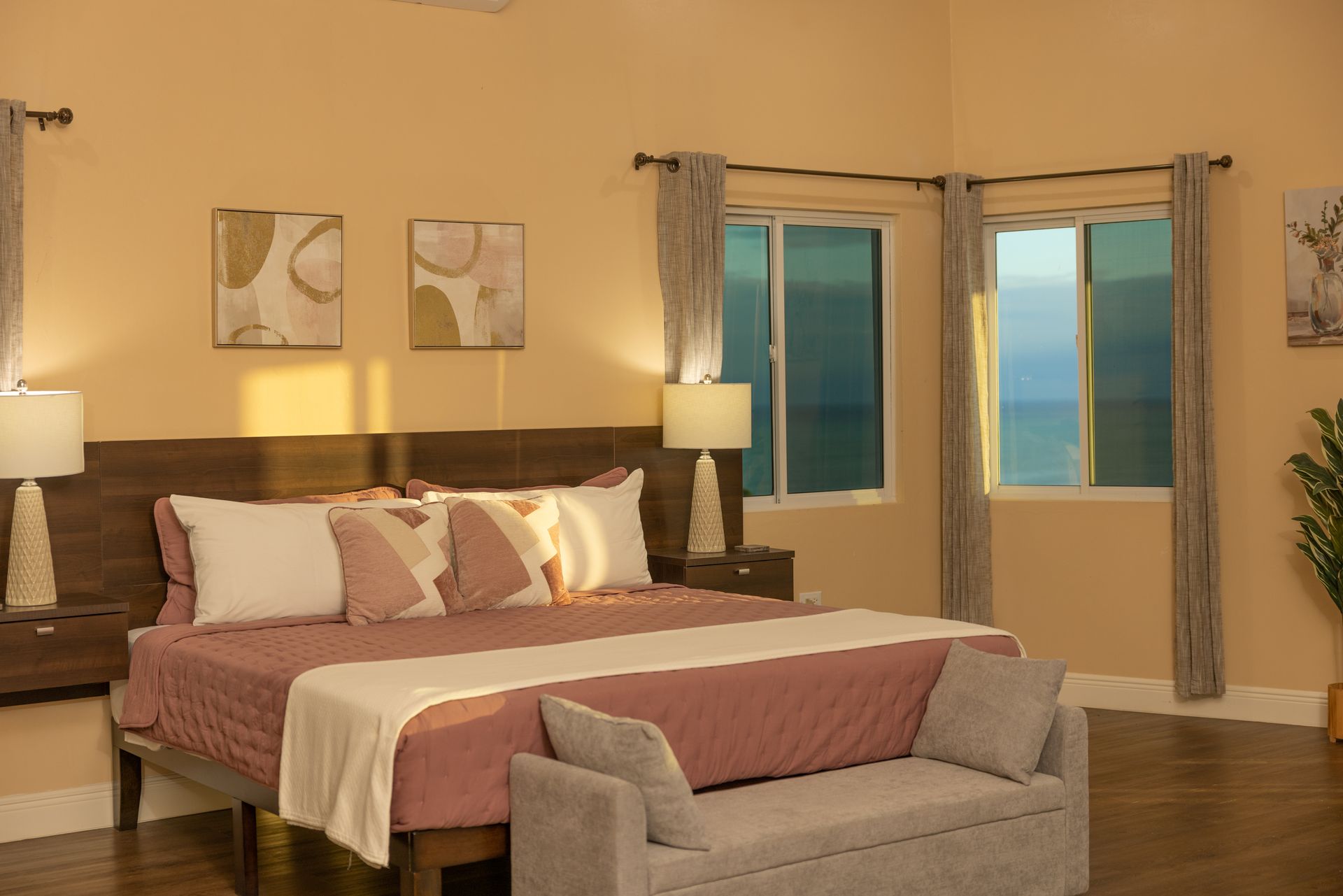 Bedroom with a bed, bench, windows, and two bedside tables. The room is painted yellow.