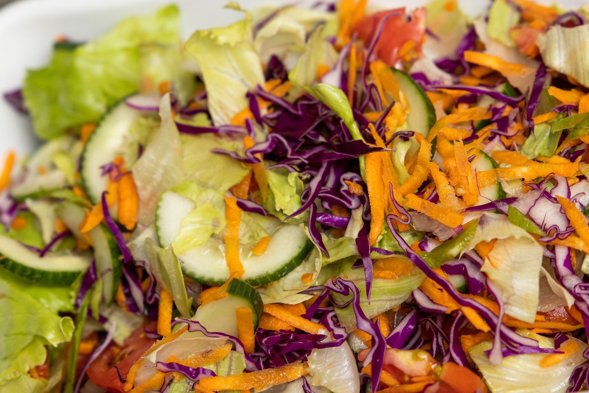 Salad with shredded carrots, red cabbage, cucumbers, and lettuce; close-up.
