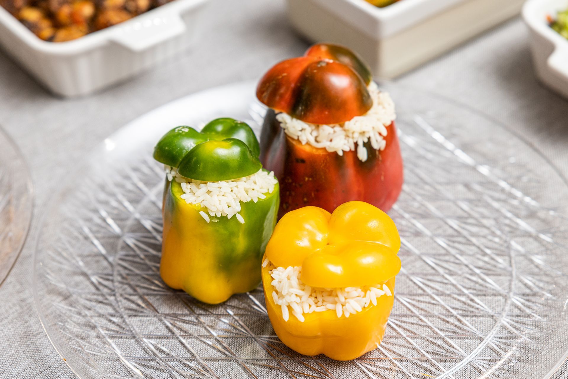 Stuffed bell peppers in yellow, green, and red on a clear plate.