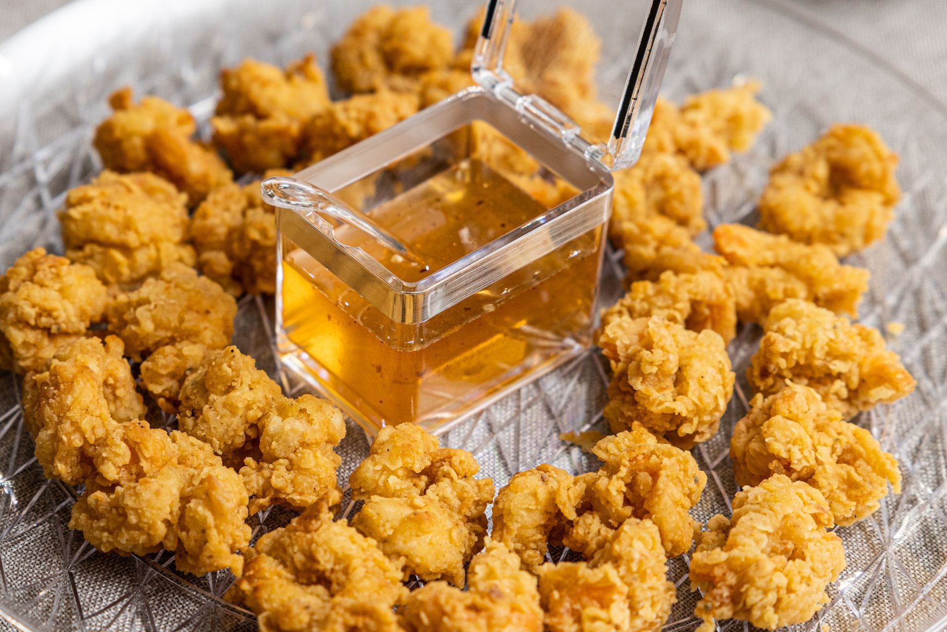 Golden fried chicken bites with dipping sauce in a clear container.