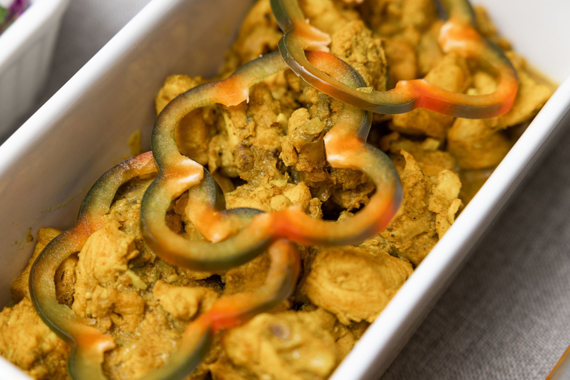 Chicken curry with green and orange bell pepper slices in a white rectangular dish.