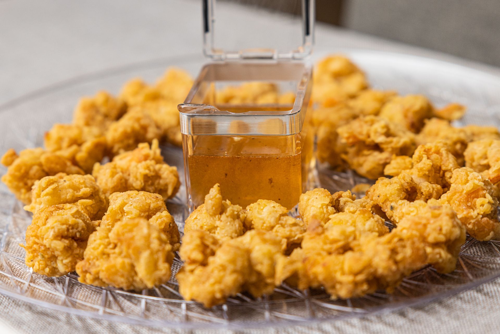 Fried chicken nuggets arranged around a square container of dipping sauce on a clear plate.