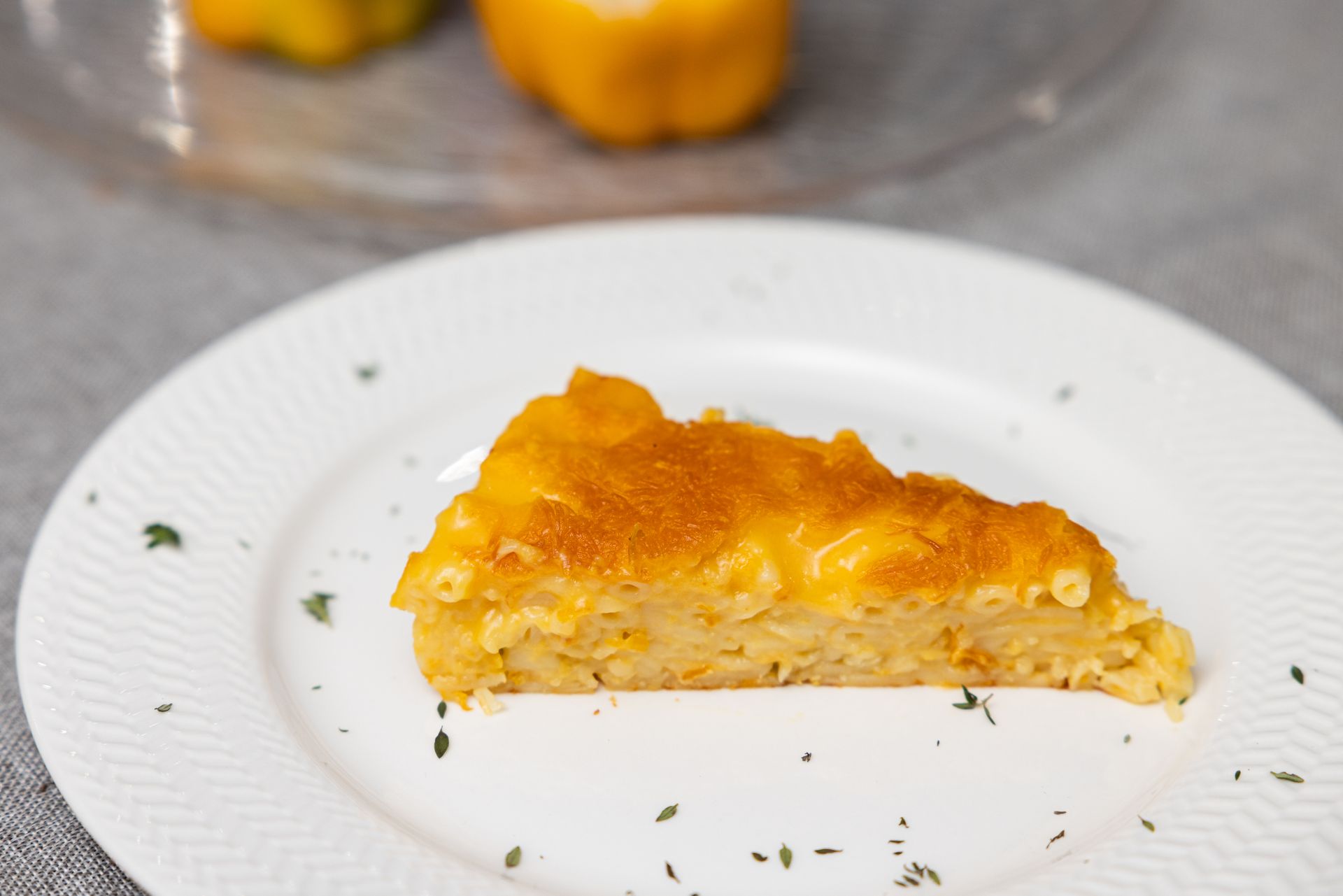 Slice of baked mac and cheese on a white plate, topped with melted cheddar, garnished with herbs.