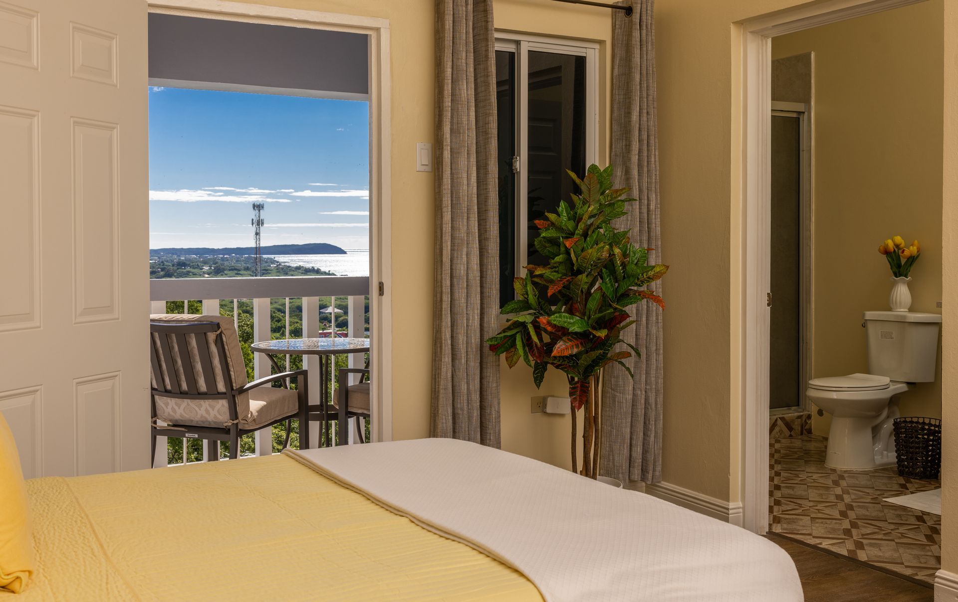 Bedroom with balcony overlooking water; includes bed, table, chairs, and bathroom.