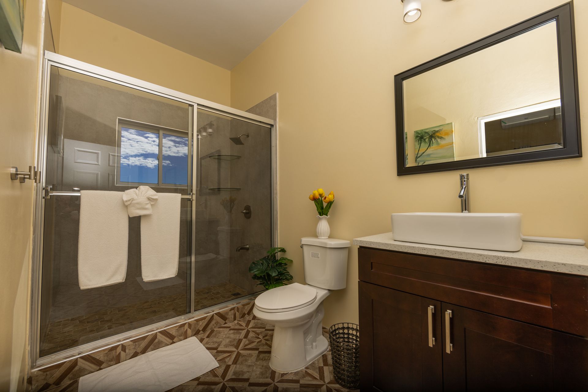 Bathroom with glass shower, toilet, sink, and dark wood vanity; tan walls, brown and tan tile.