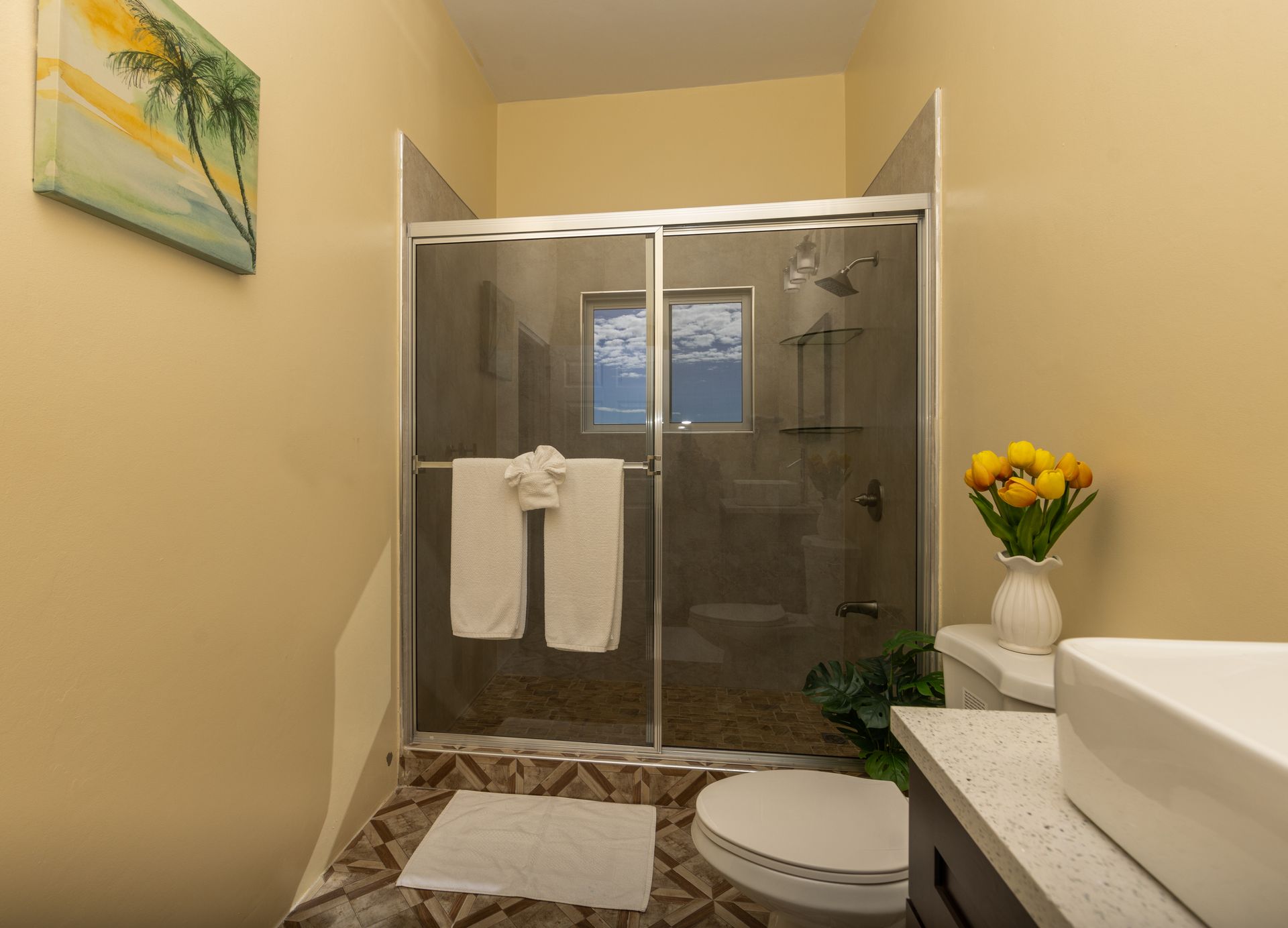 Bathroom with glass shower, white sink, and yellow walls.