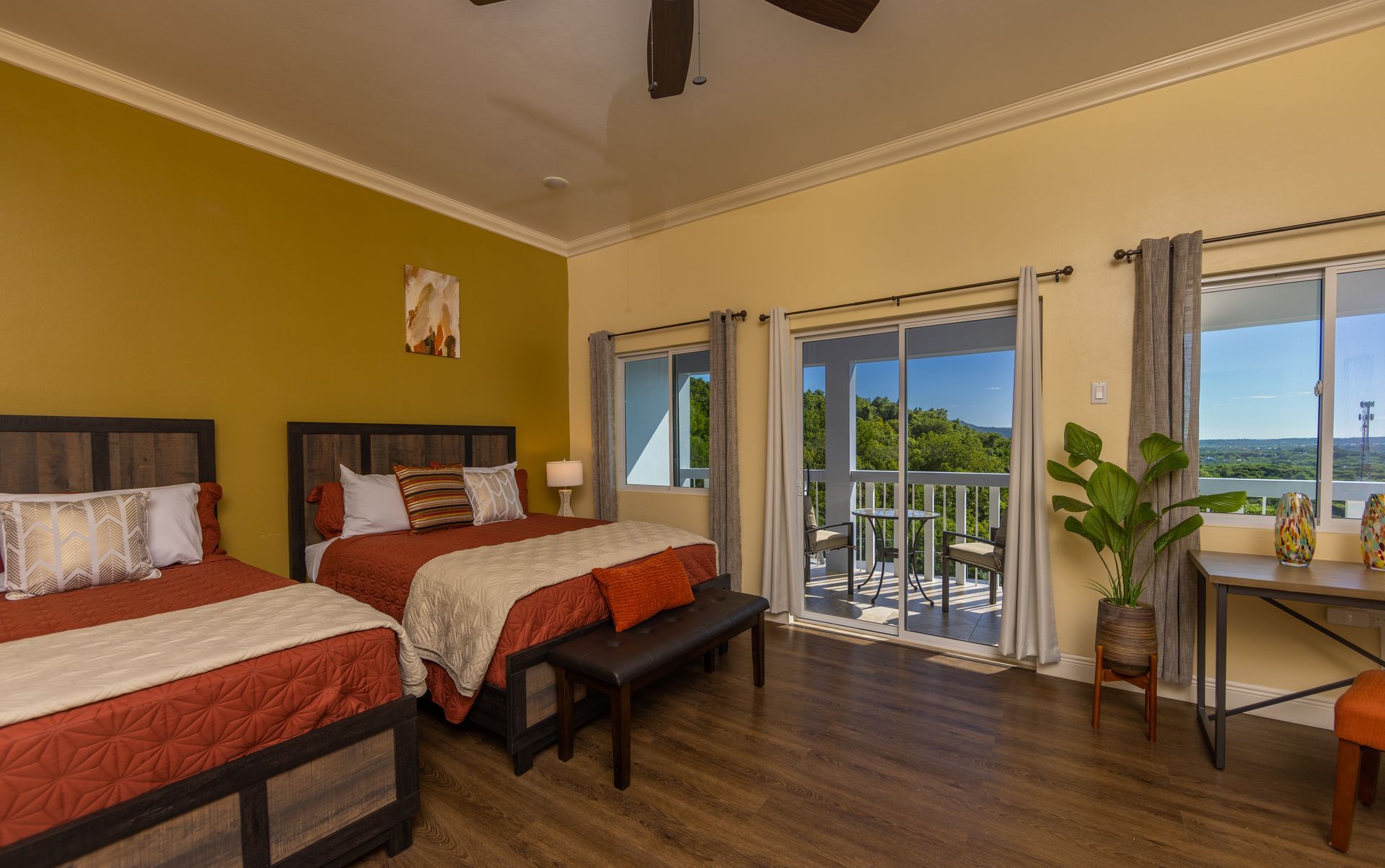 Bedroom with two beds, balcony access, and desk. Room features wood floors, yellow and orange walls.