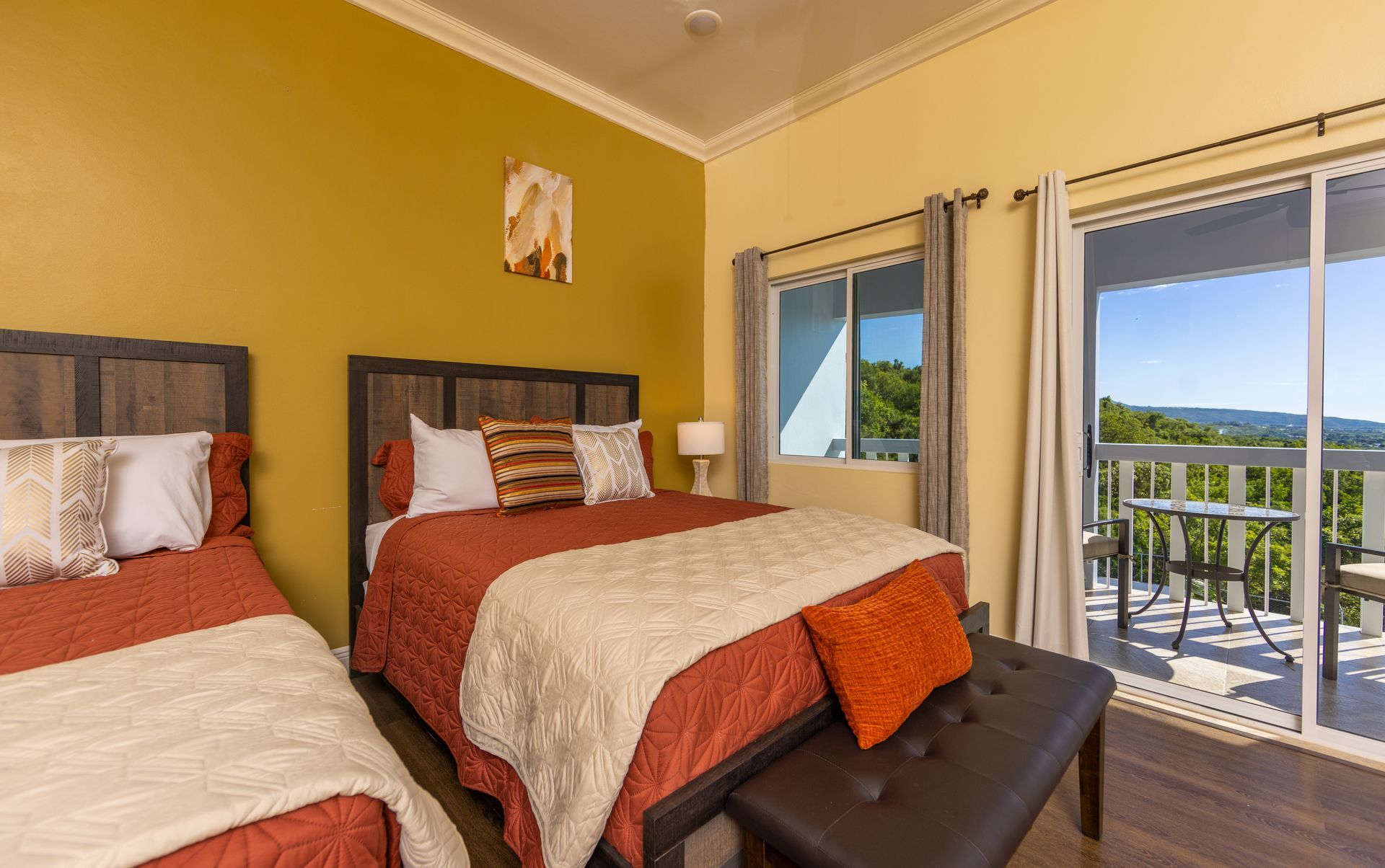 Bedroom with two beds, orange bedding, and balcony access with mountain view.