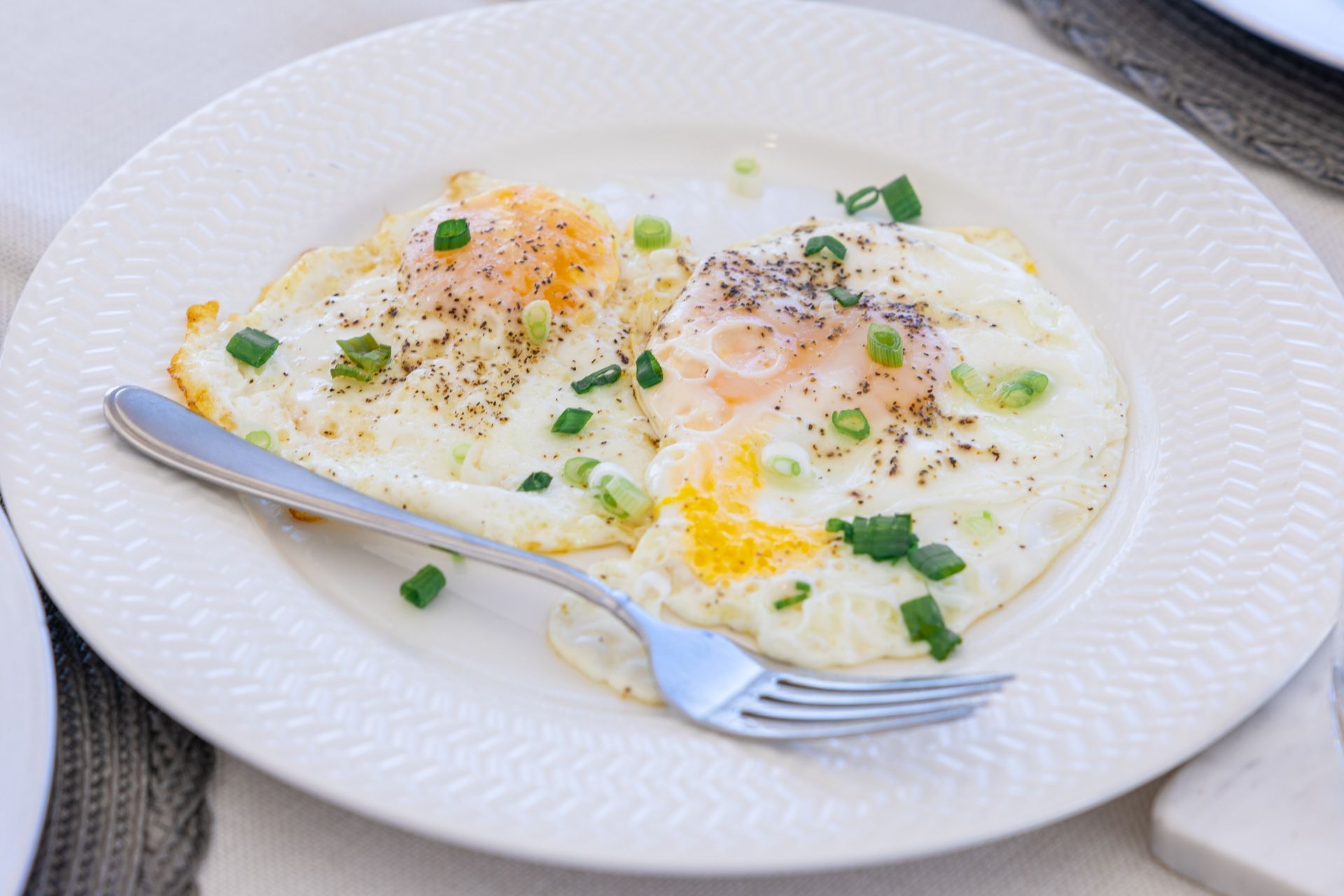 Two fried eggs on a white plate, sprinkled with green onions and pepper, with a fork.
