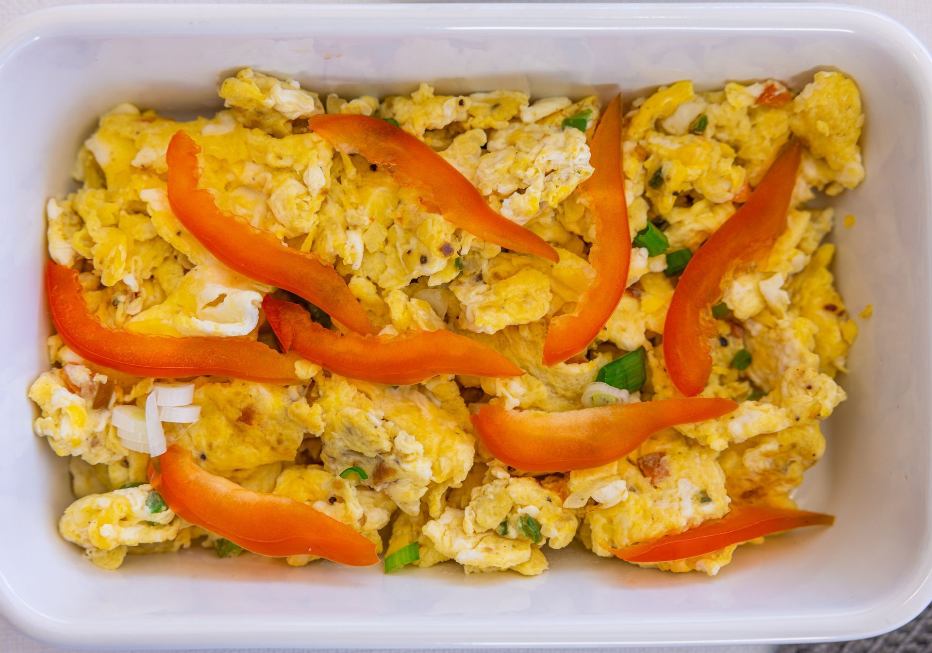 Scrambled eggs with red bell pepper strips in a white container.