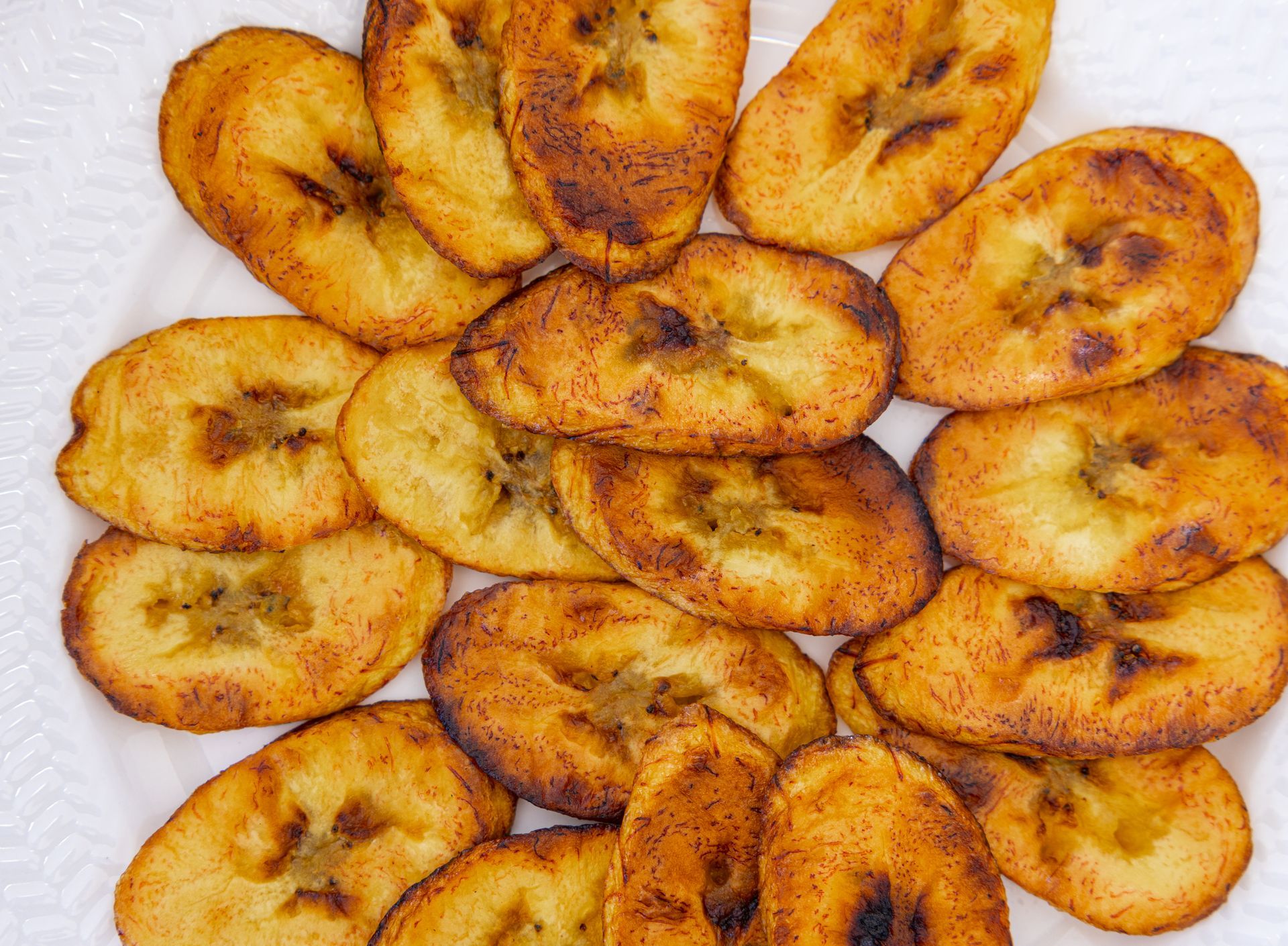 Sliced, fried plantains arranged on a white plate; golden-brown with dark edges.