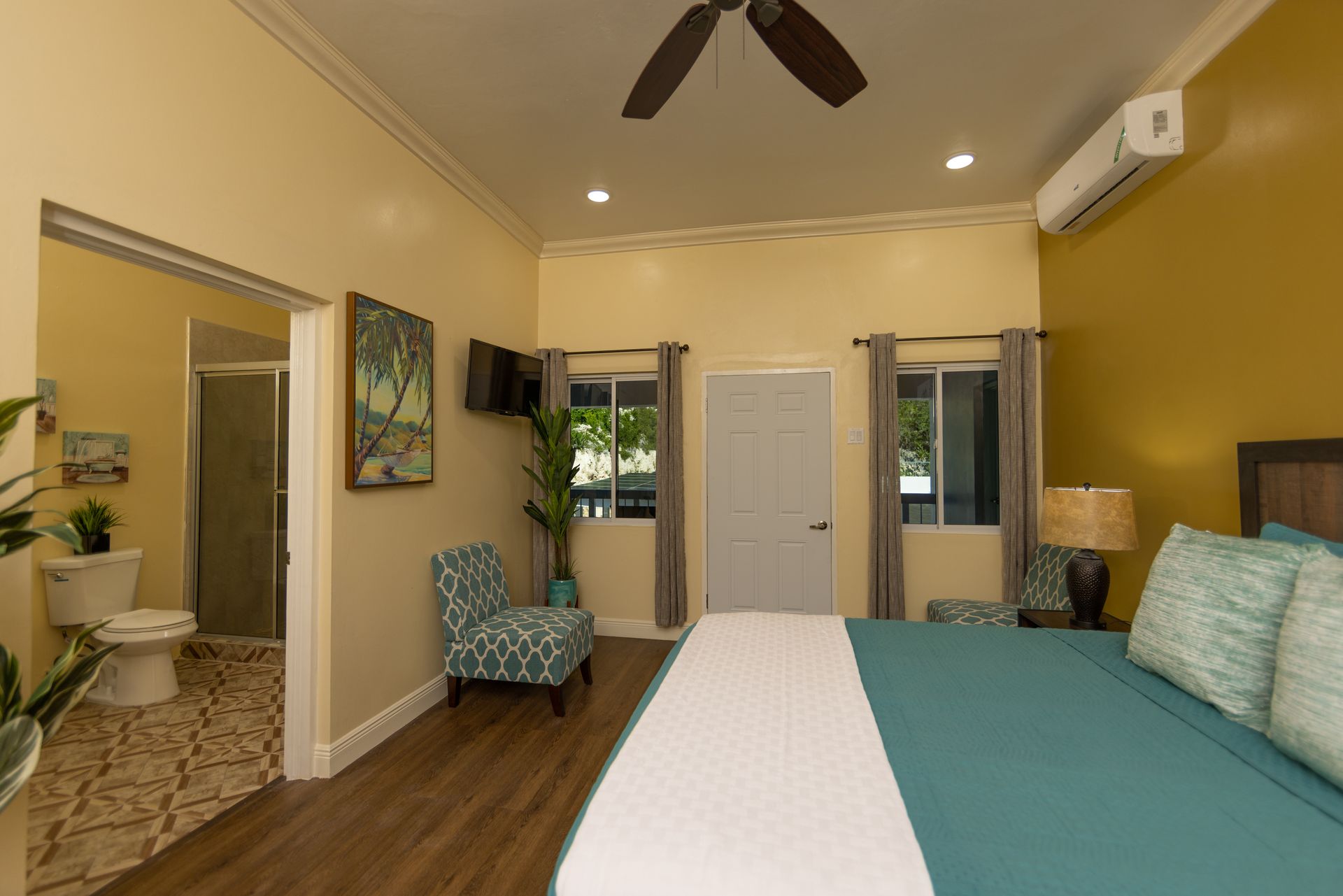 Hotel bedroom with king bed, bathroom doorway, two chairs, and a window.