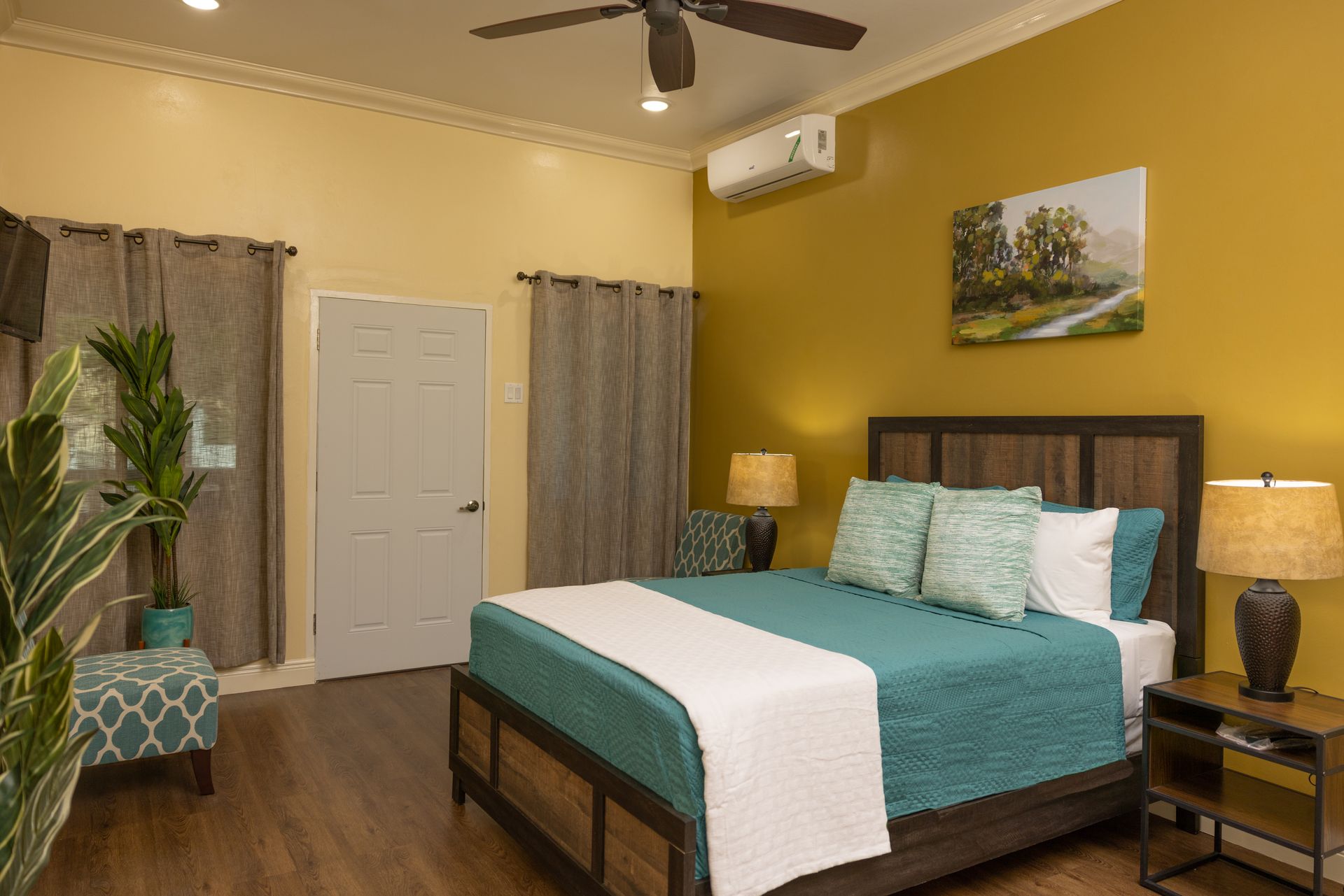 Bedroom with teal bedding, wood furniture, yellow walls, and a painting.