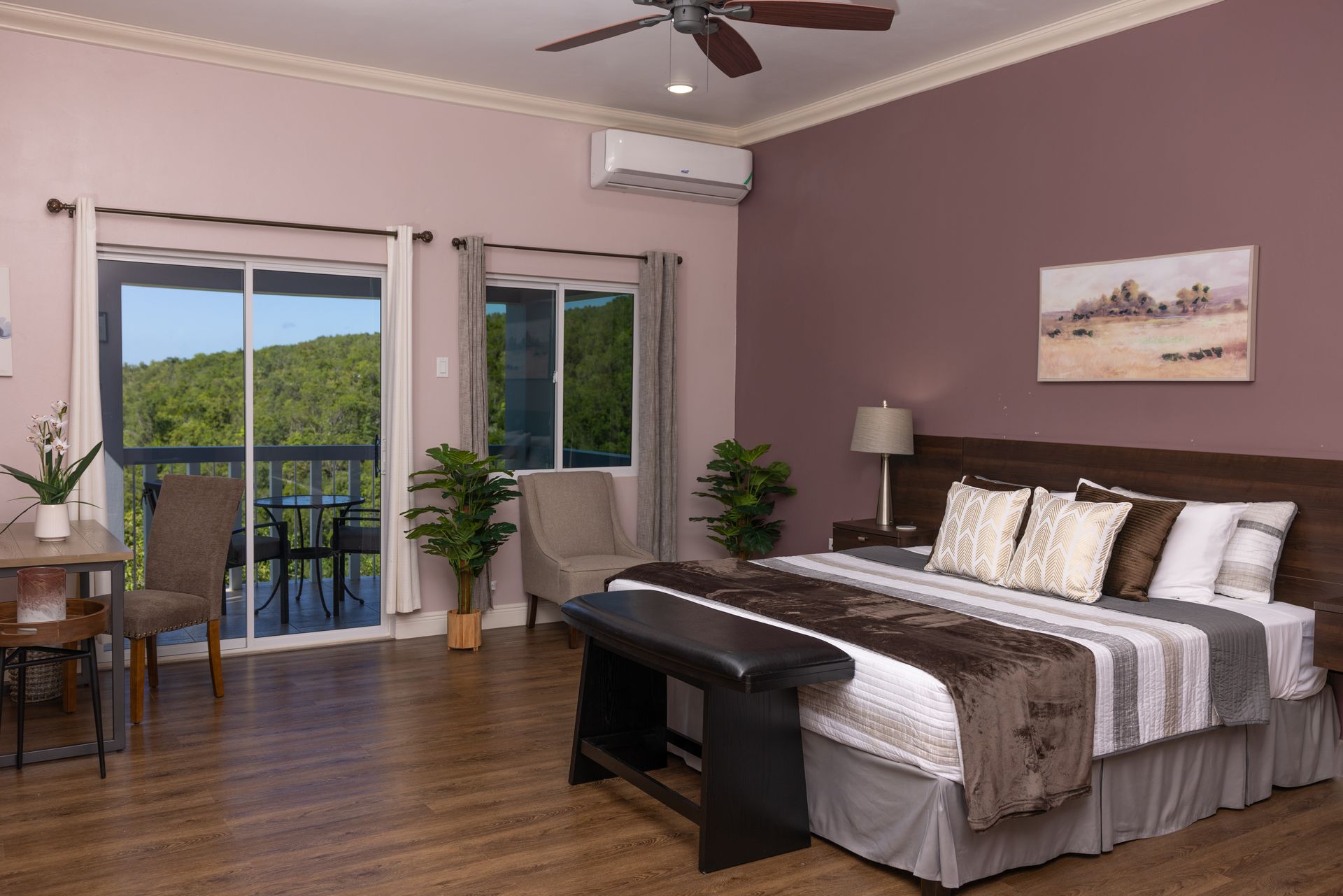 Bedroom with bed, balcony view, mauve walls, plants, wood flooring.