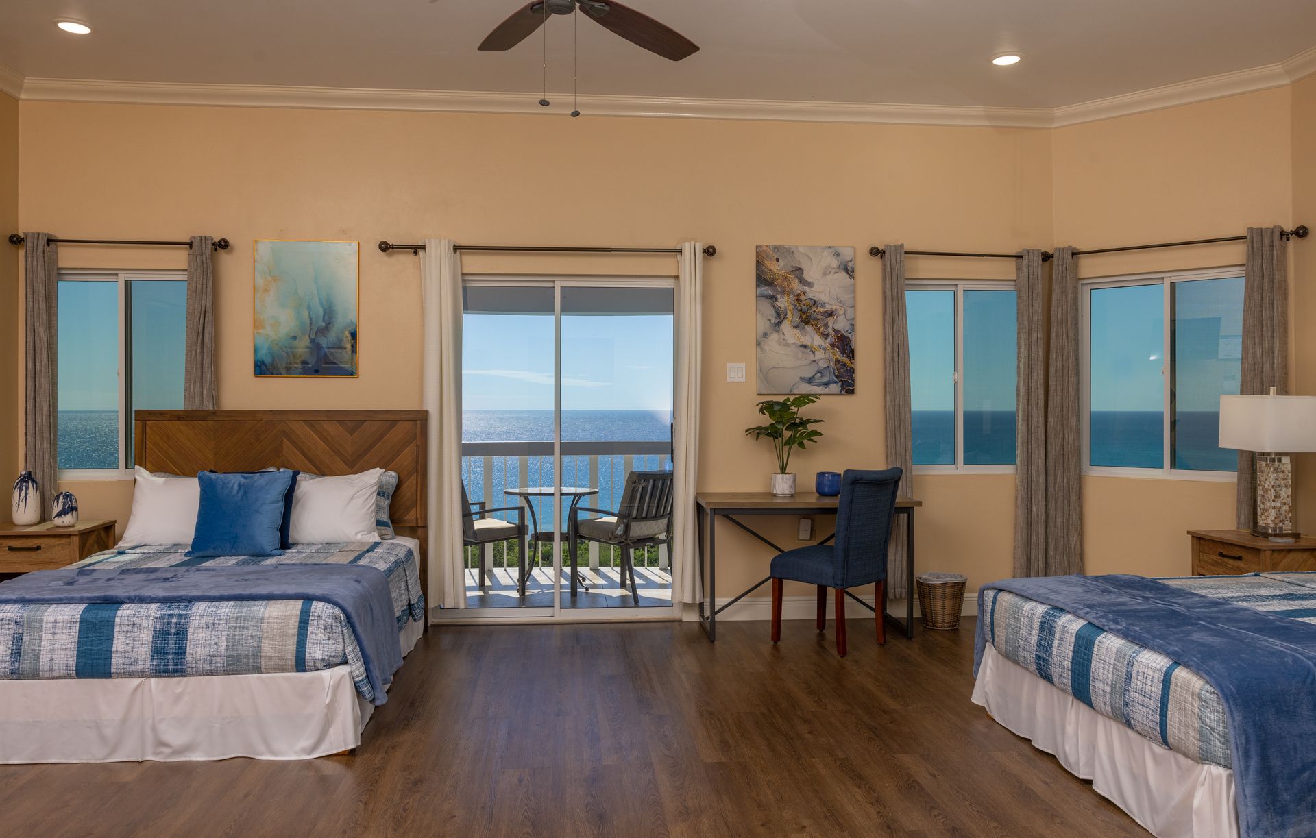 Spacious bedroom with two beds, a balcony overlooking the ocean, and art on the walls.