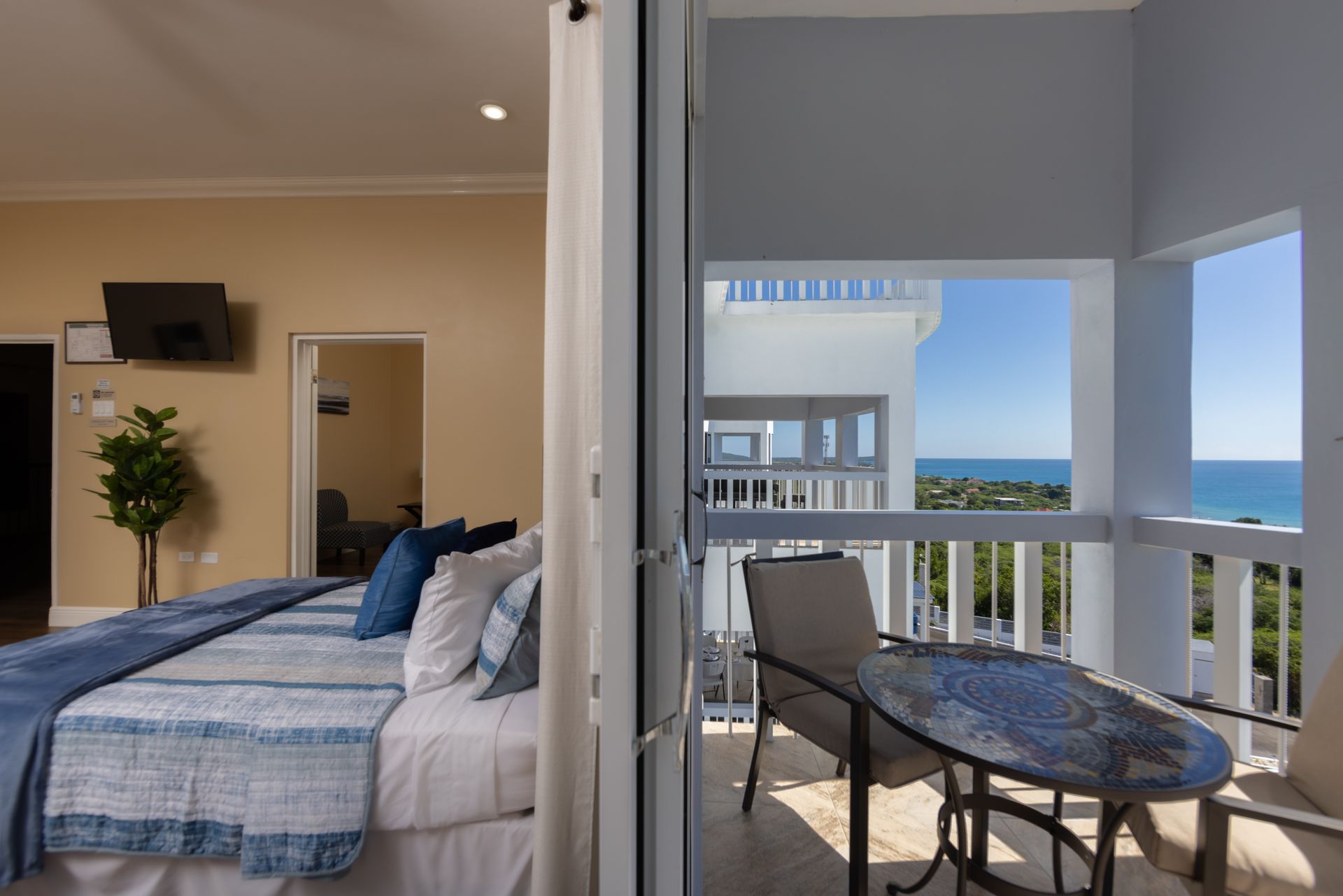 Bedroom interior with balcony overlooking the ocean; bed, small table, and chairs.