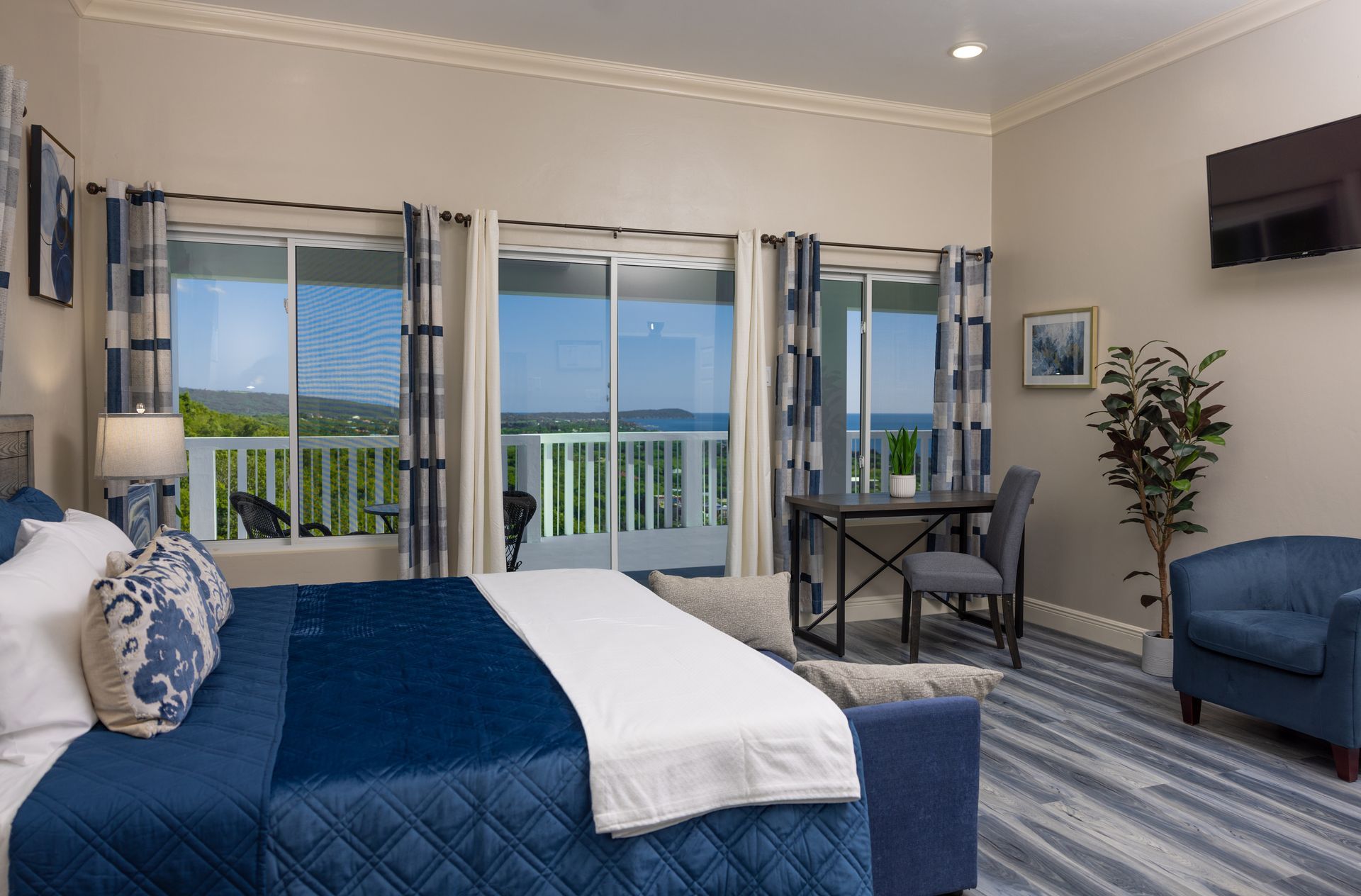 Bedroom with a blue bed, ocean view balcony, desk, and armchair.