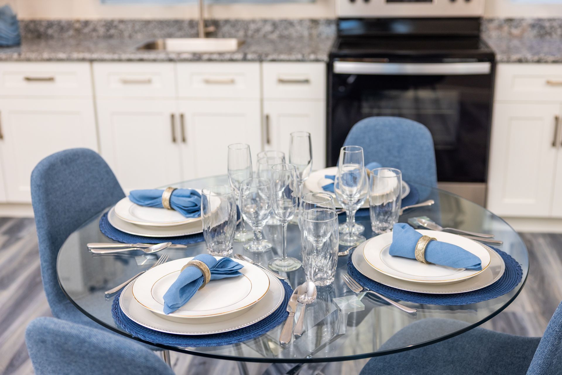 Dining table set for four with blue accents and white kitchen background.