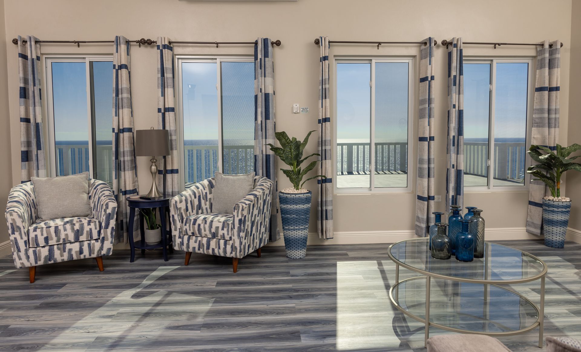 Living room with ocean view, blue and white patterned curtains, armchairs, and decorative plants.