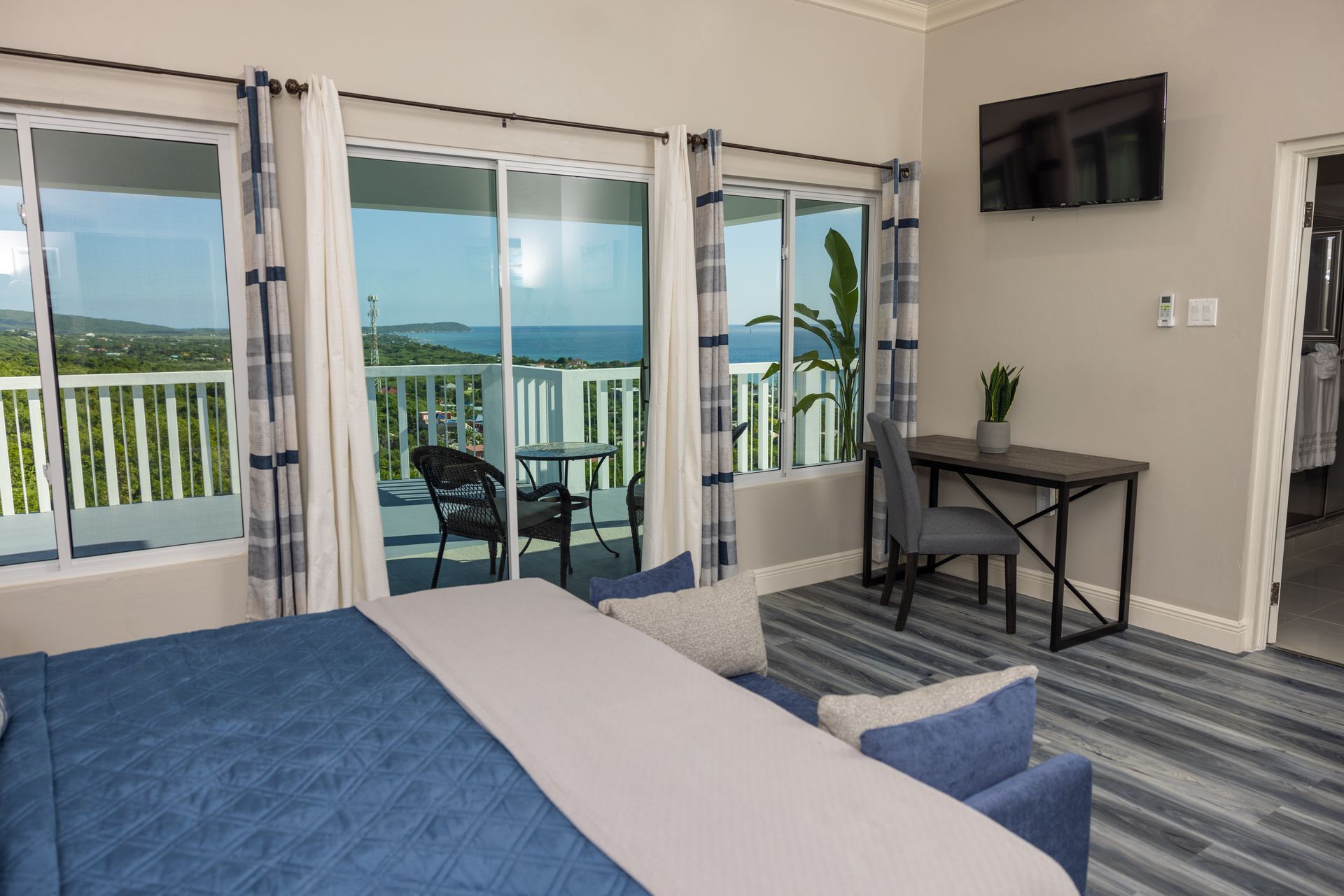 Bedroom with ocean view, sliding glass doors, balcony, bed, desk, chair, and TV.