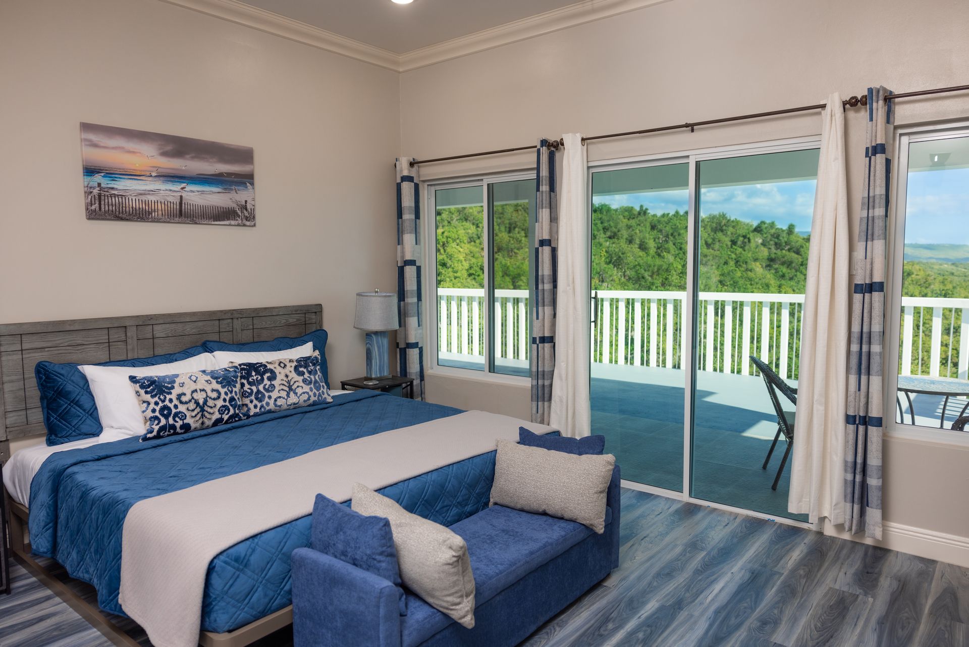 Bedroom with king bed, balcony view, blue and white decor.