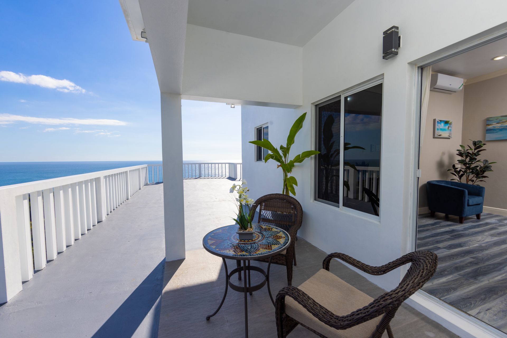 Balcony with ocean view, table, chairs, and potted plant, sunny sky.