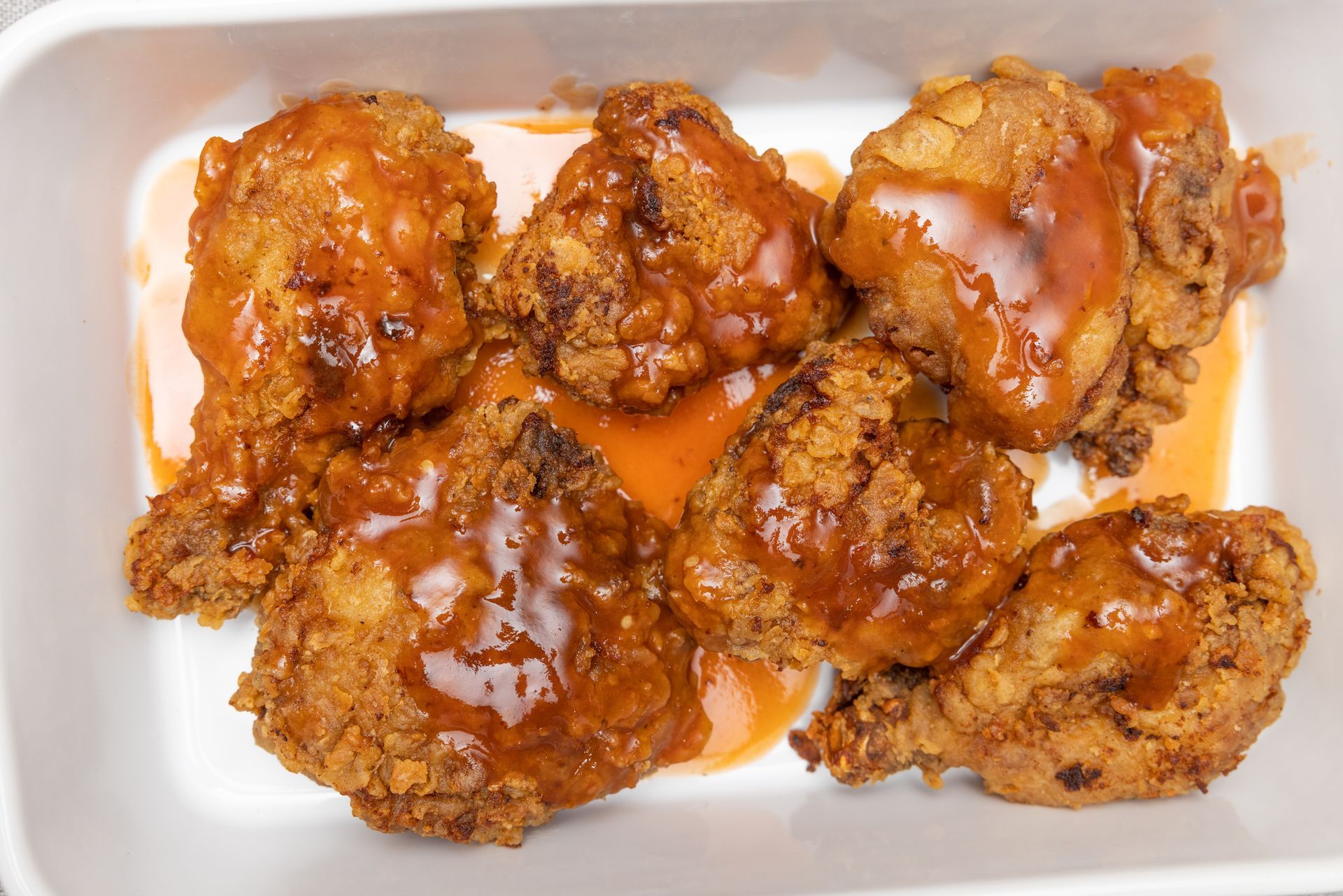 Fried chicken pieces in a white container, coated in orange sauce.