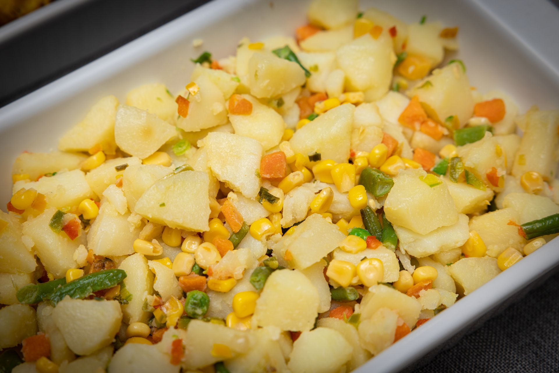 Potato salad with corn, carrots, and green beans in a white dish.