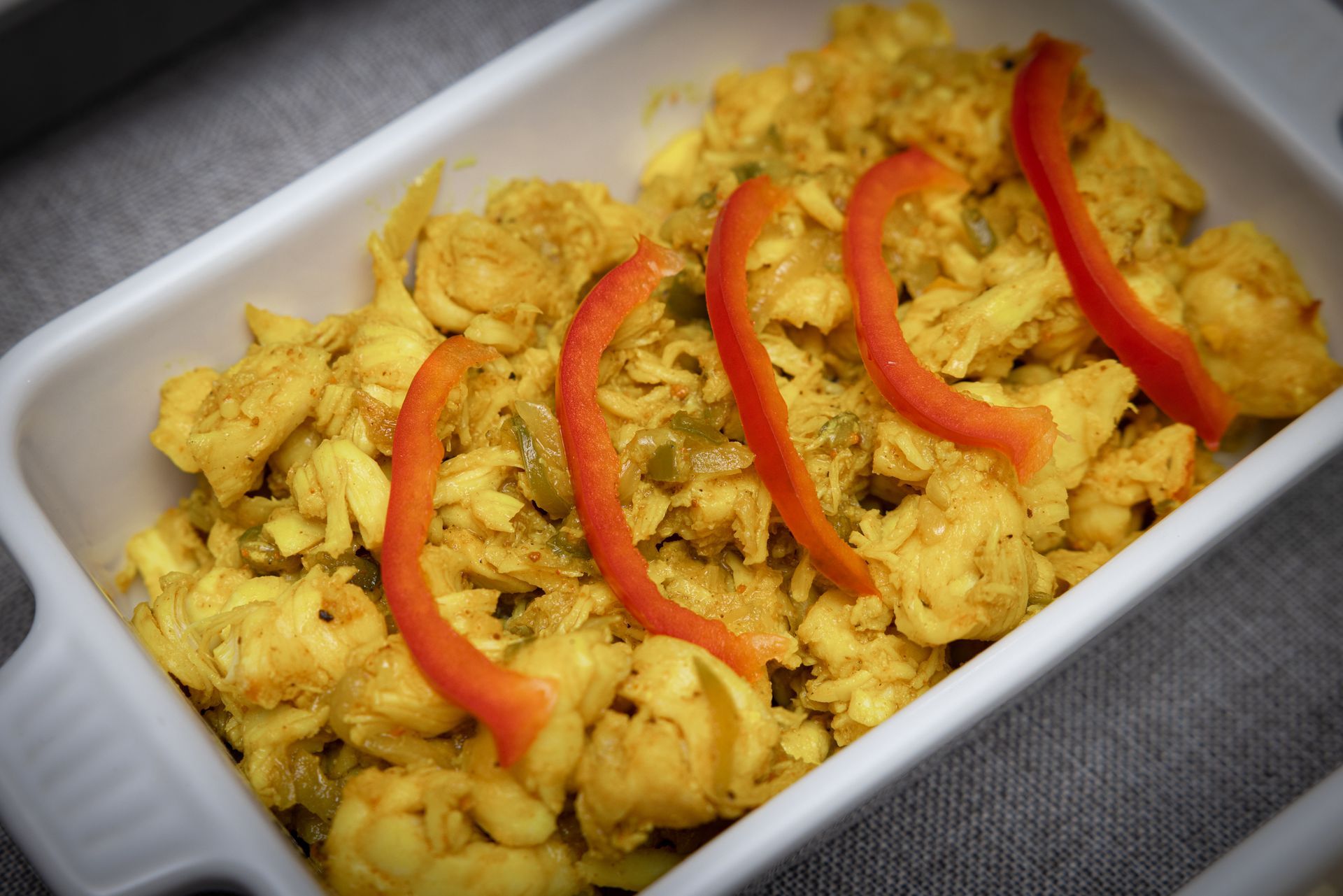 Curried chicken dish in a white rectangular serving dish, garnished with red pepper strips.
