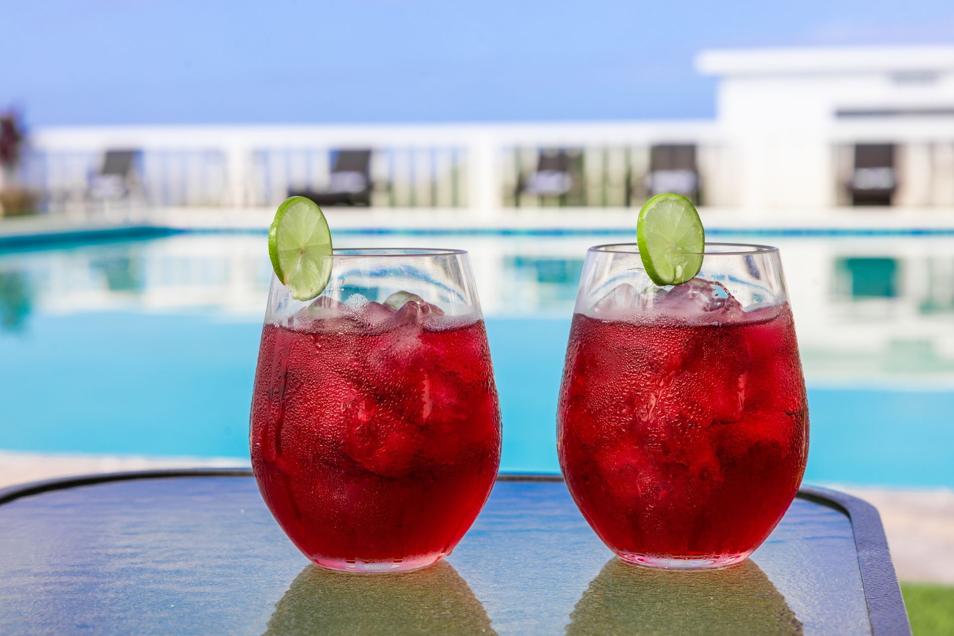 Two red cocktails with lime slices by a pool.