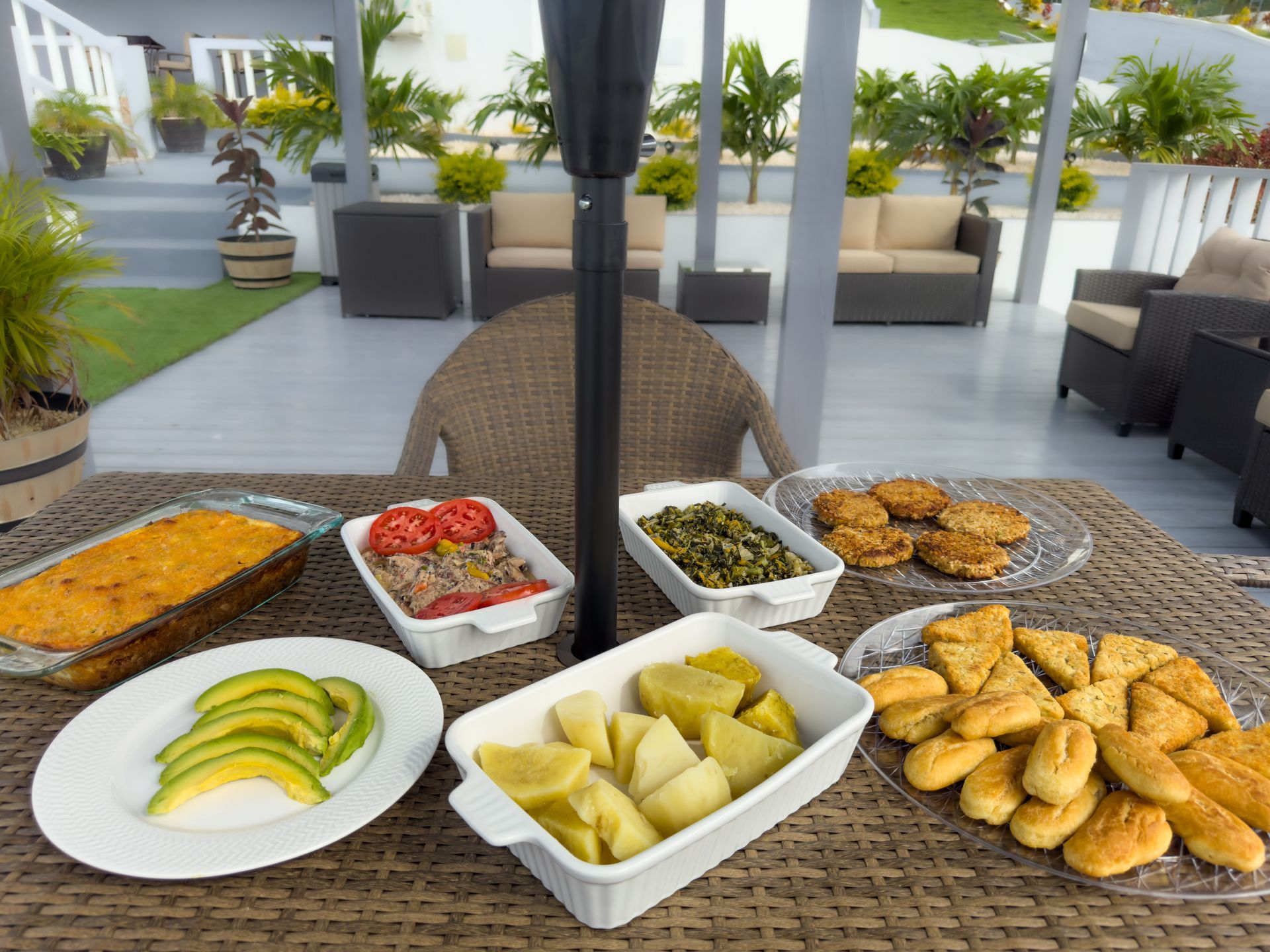 A table laden with Caribbean dishes: casserole, avocado, tuna salad, callaloo, dumplings, and bread.