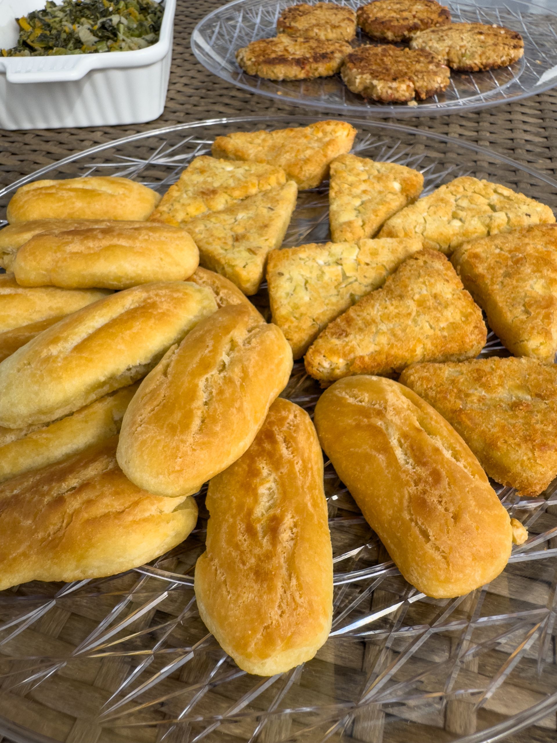Assorted golden-brown baked goods, including rolls and triangular and square shapes, are arranged on a clear wire rack.
