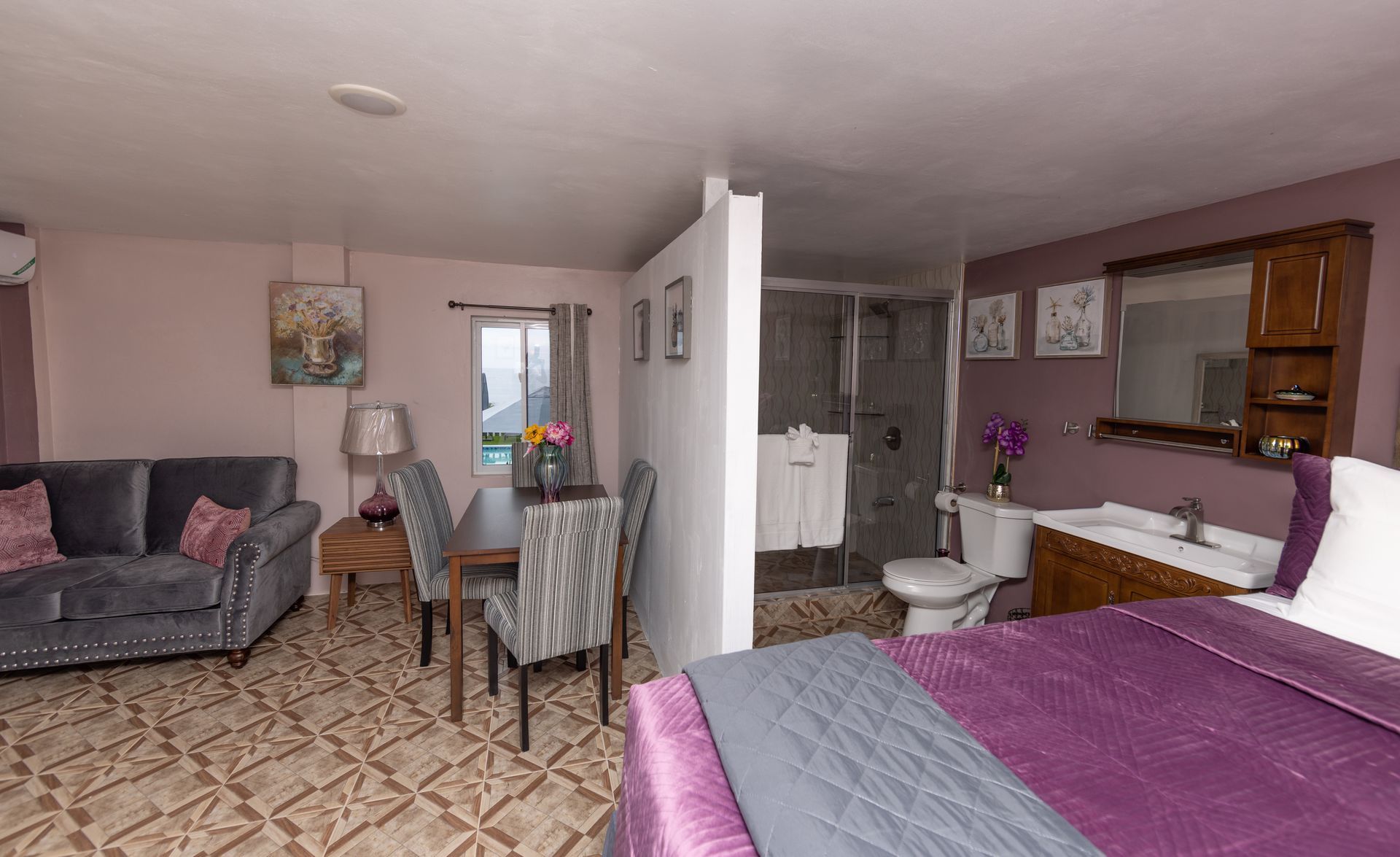 Studio apartment with living, dining, and sleeping areas; bathroom partition. Purple, gray, and wooden accents.