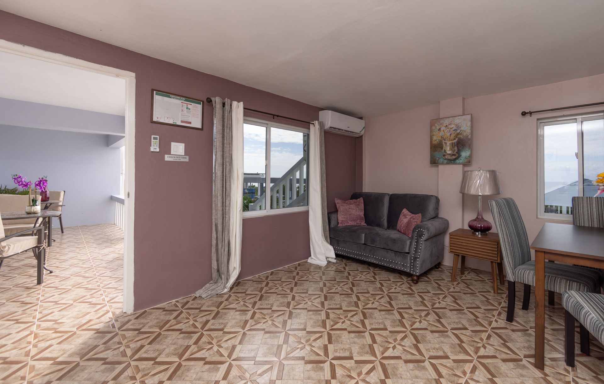 Living room with grey sofa, patterned tile floor, open door to dining area, window view.