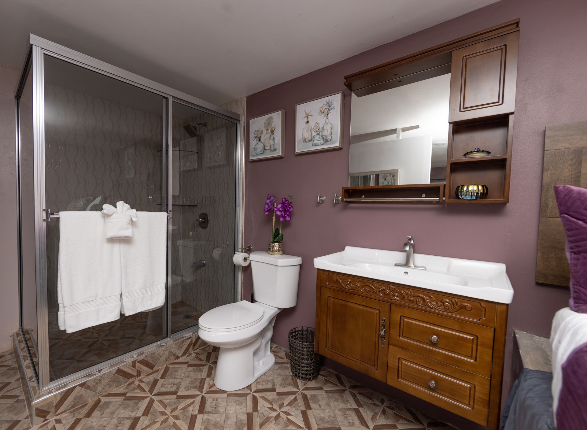Bathroom with a glass shower, toilet, and wooden vanity against a purple wall.
