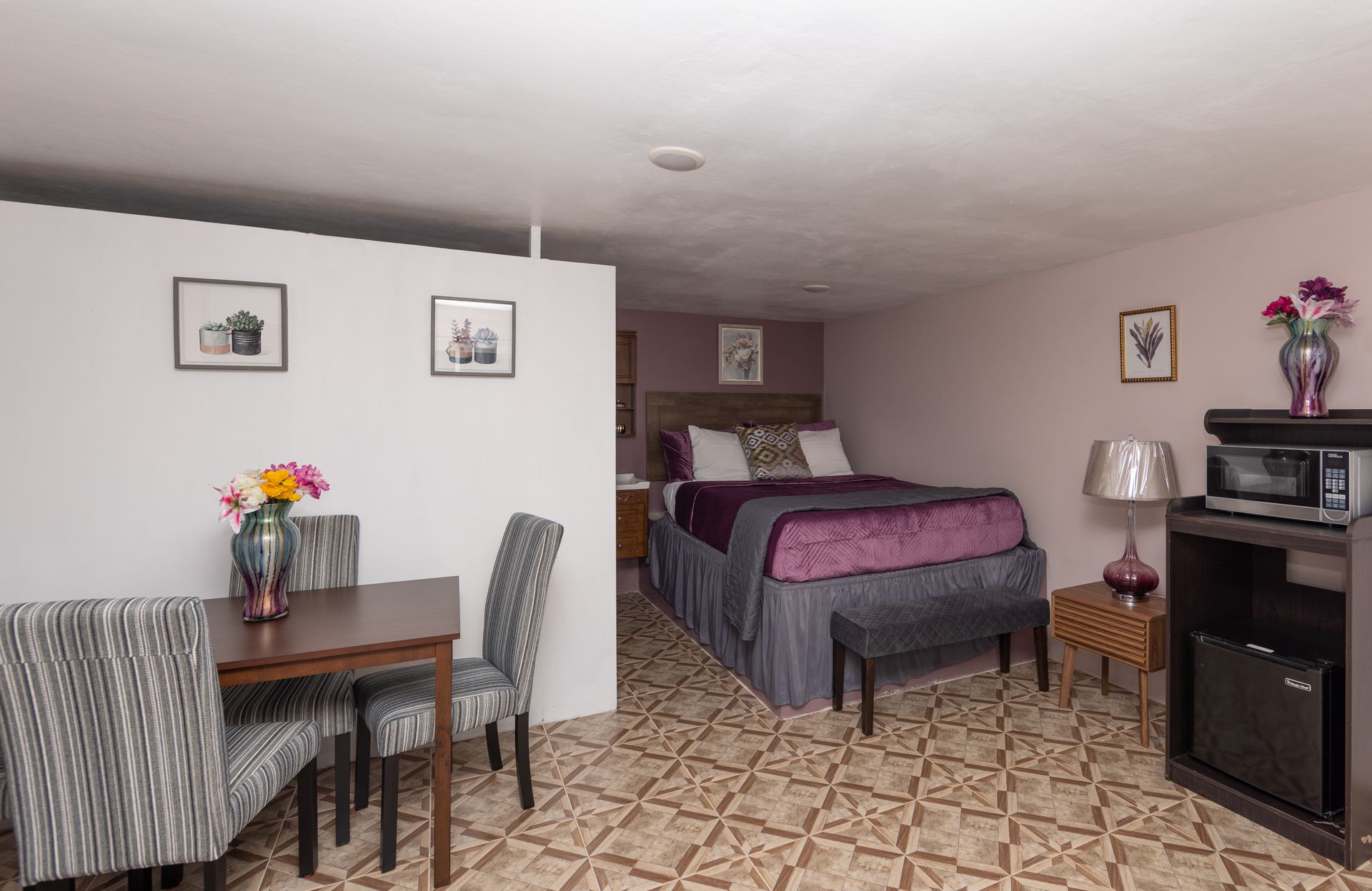 Small hotel room with bed, table, chairs, microwave, and decor.