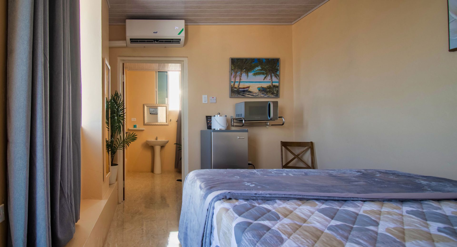 Cozy bedroom with bed, microwave, mini-fridge, and view of a bathroom. Neutral tones and natural light.