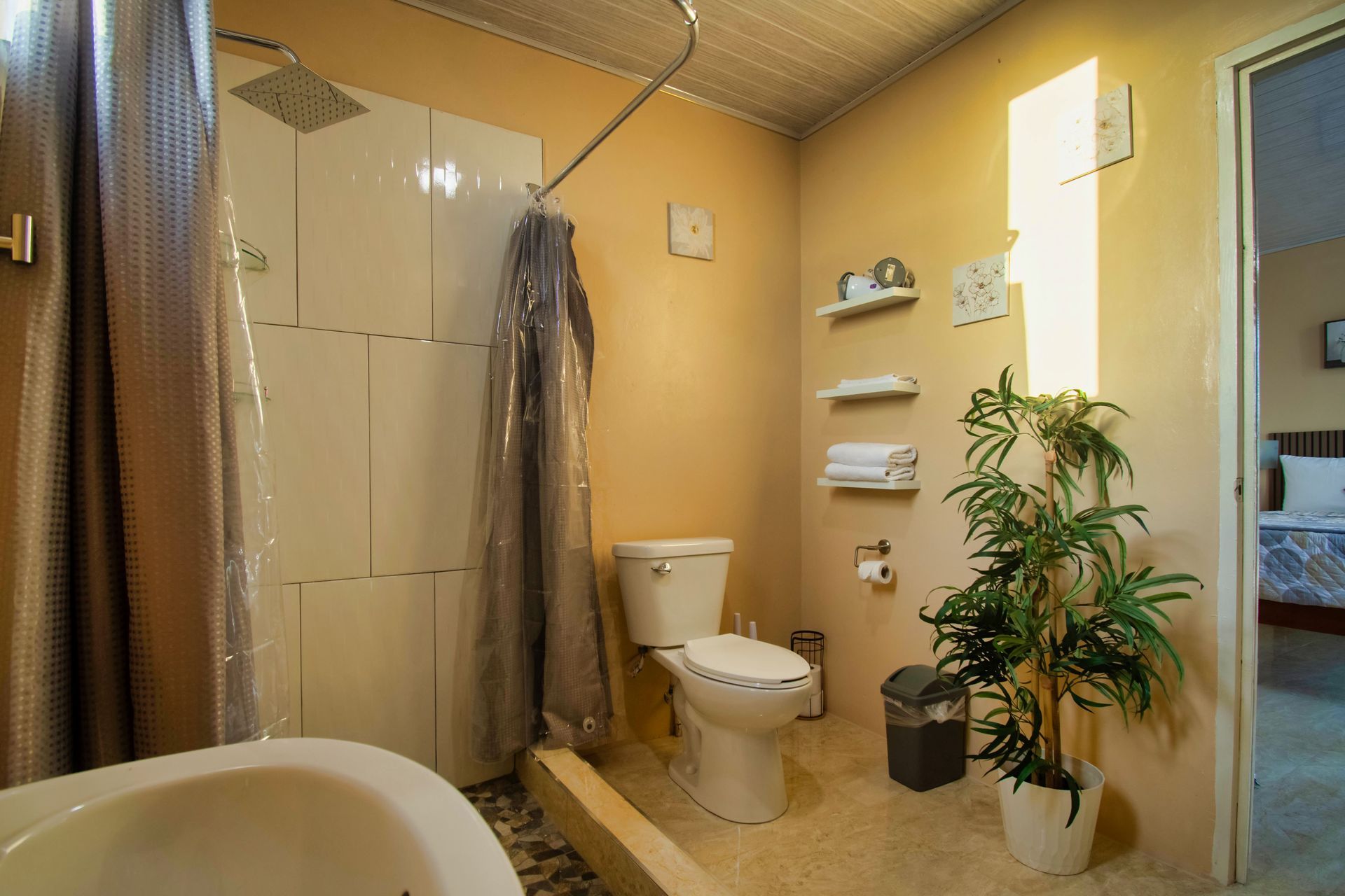 Bathroom with shower, toilet, and plant. Light beige walls, white shower, and beige floor.