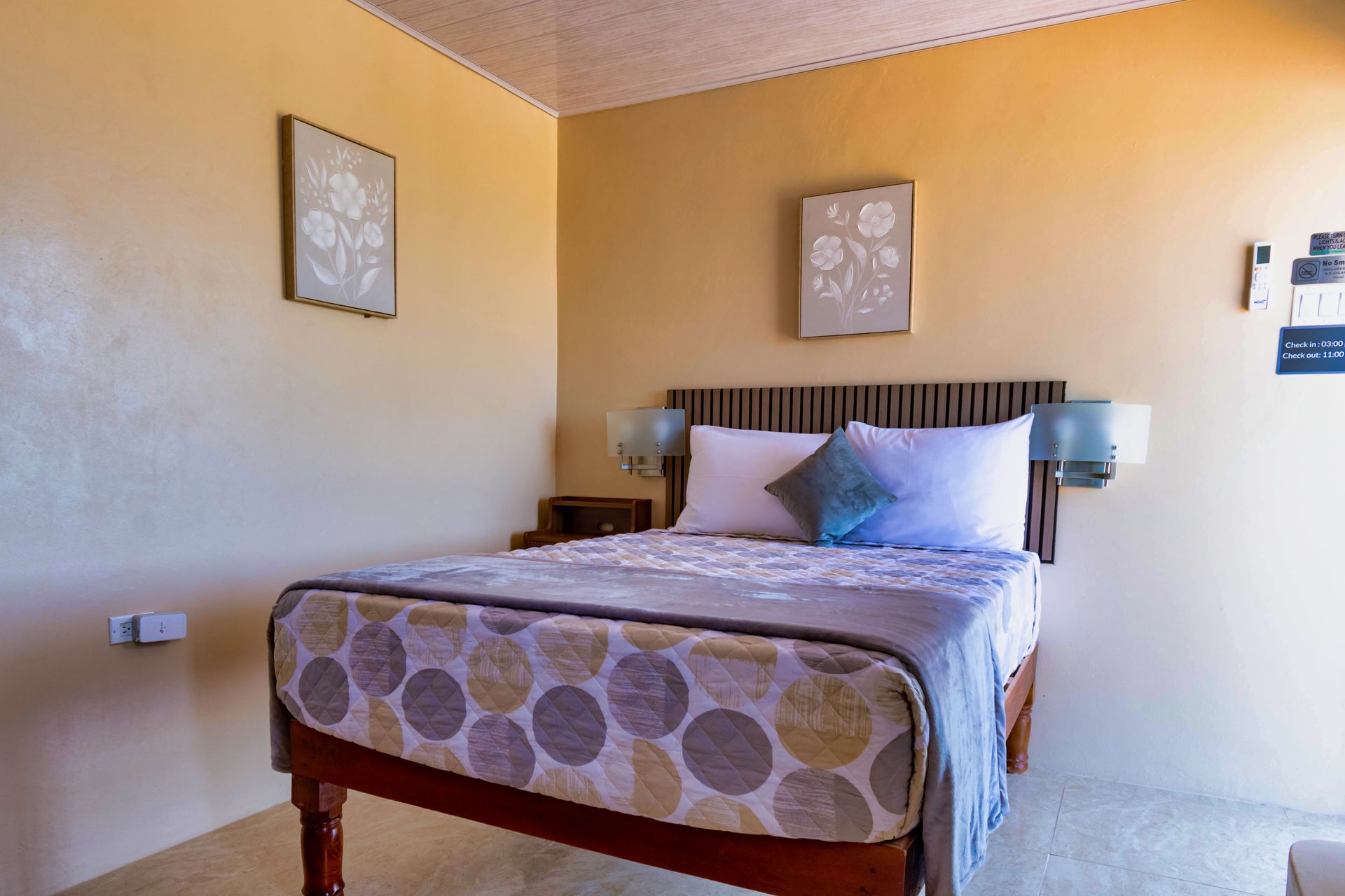 Bedroom with a bed, nightstands, and floral wall art; light yellow walls and wooden furniture.