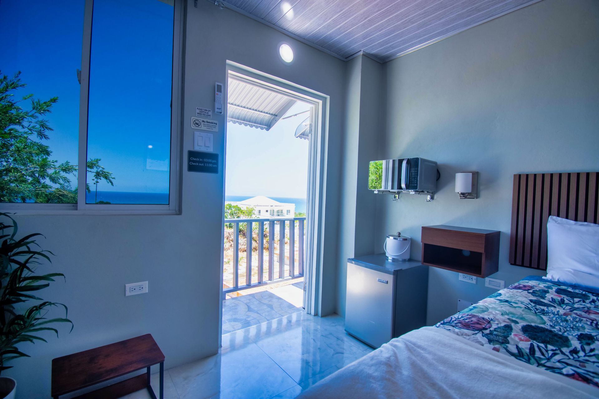 Bedroom with a bed, open door to a balcony, and a window with a view of the ocean.
