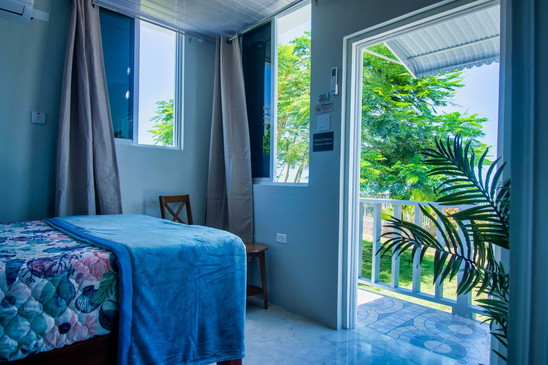 Bedroom with bed, windows, and open door to balcony with trees.