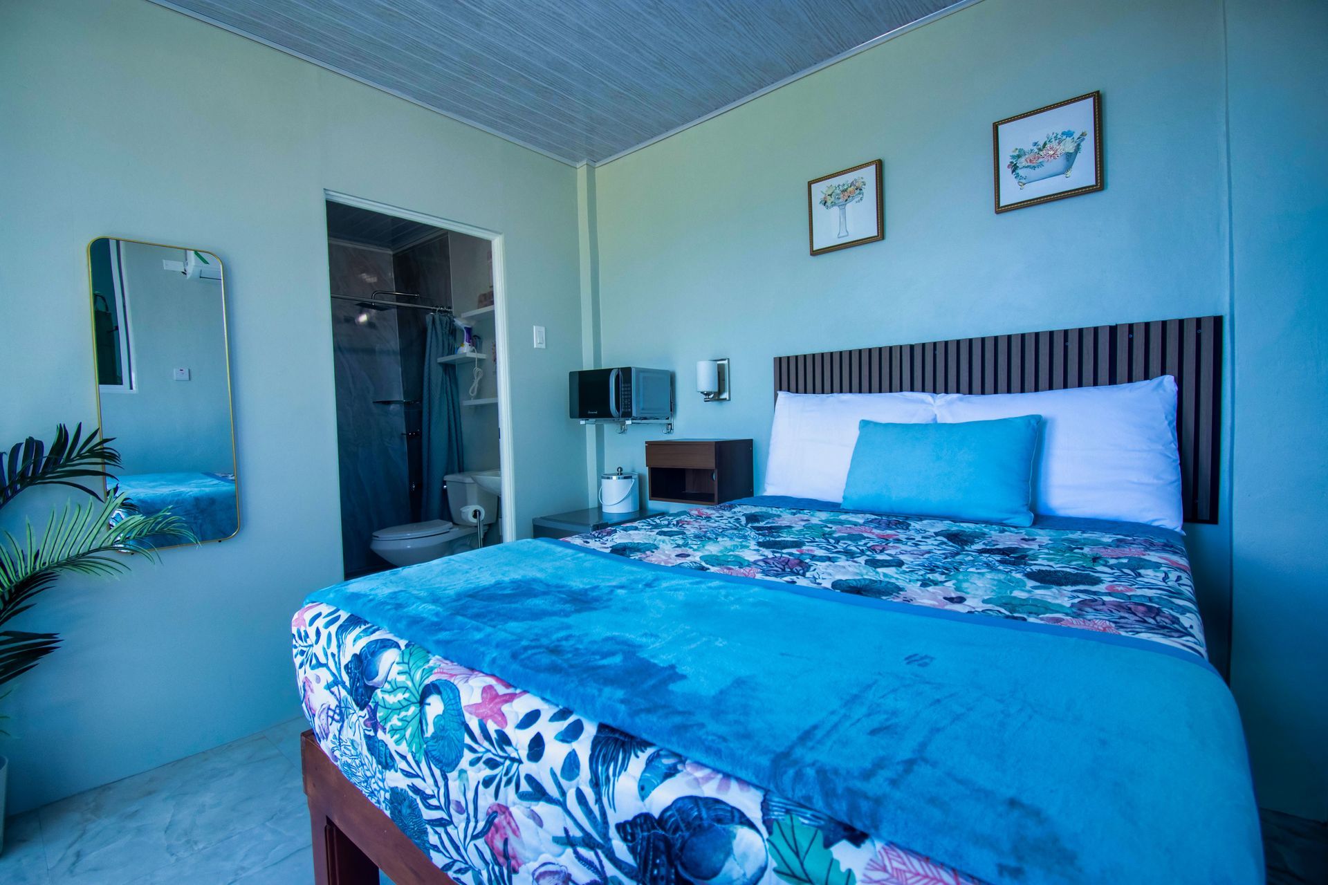 Bedroom with bed, bathroom, mirror, and two framed pictures on the wall. Light blue and green colors.